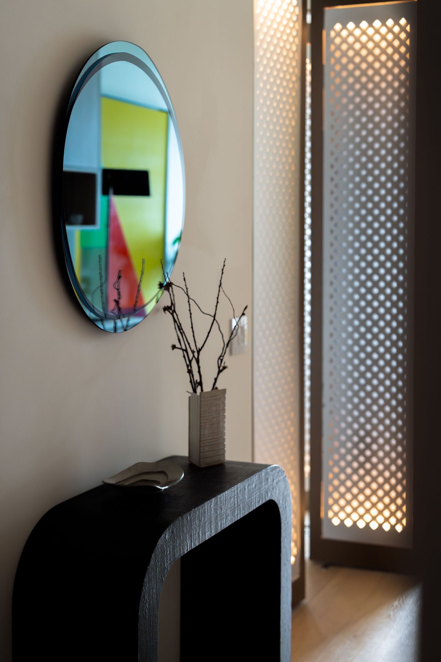 Stylish entryway with oval mirror, black console table, branch vase, and illuminated lattice panel.