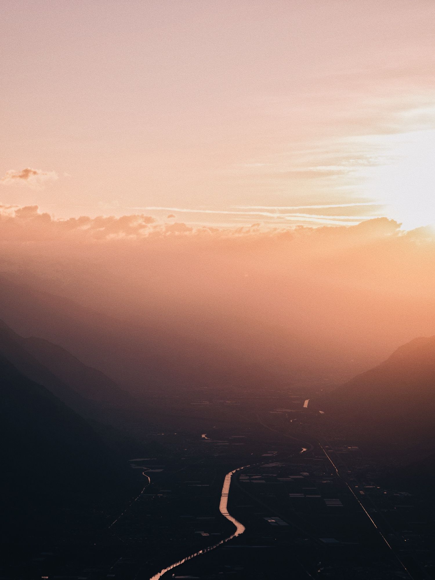 Aerial sunset view of a winding road through a mountain valley bathed in warm golden light.