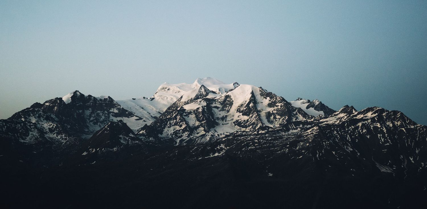 Snow-capped mountain peaks rise dramatically against a clear blue sky in this stunning alpine landscape panorama.
