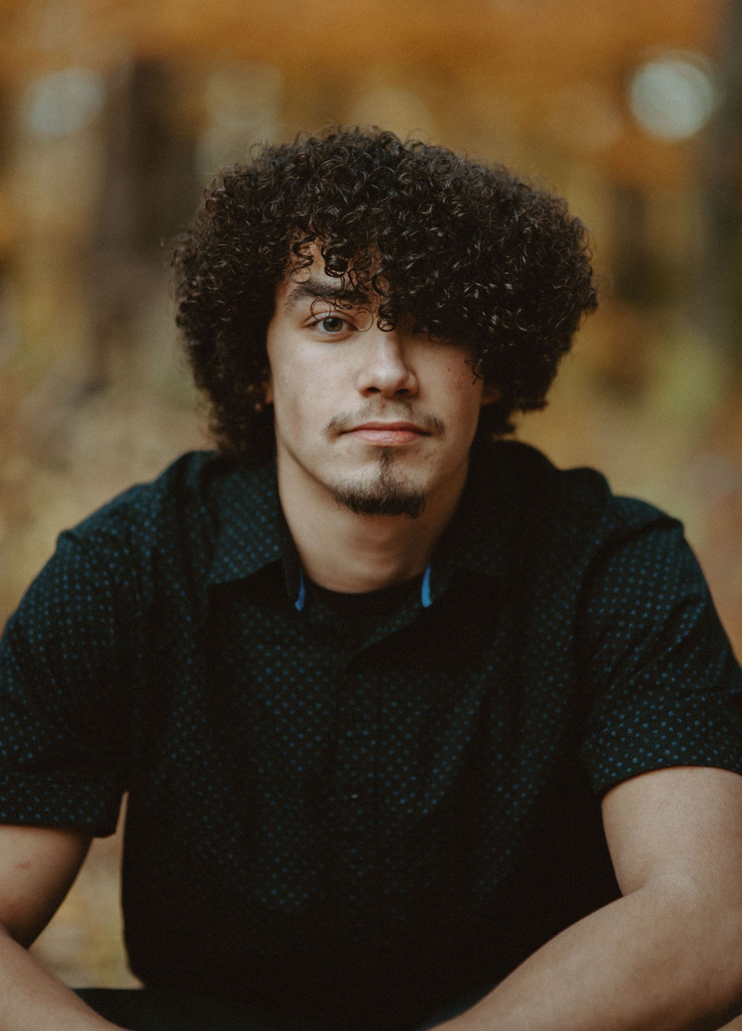 Close-up portrait of young man with curly hair in autumn forest setting.
