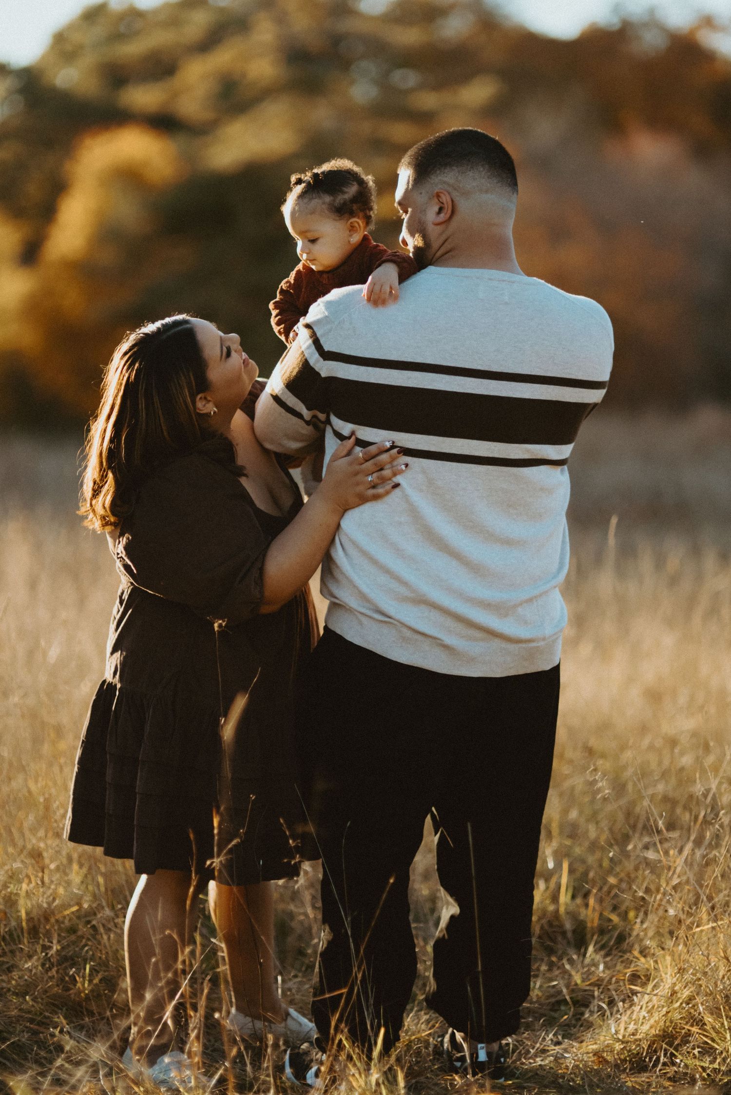 Family sharing moment with toddler in golden autumn field at sunset.