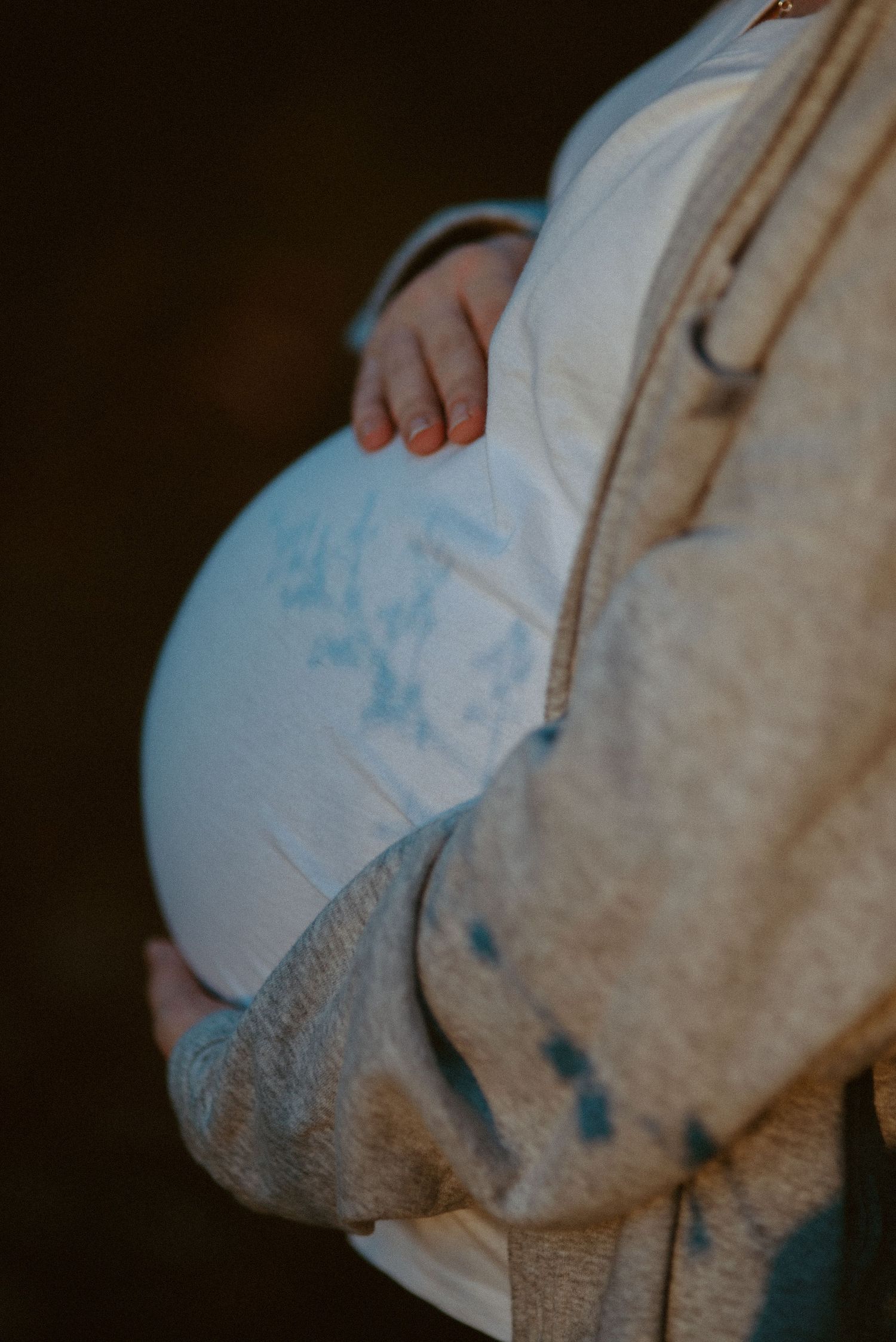 Close-up of pregnant woman cradling baby bump wearing white shirt and beige cardigan. Shadow of a flower over belly bump.