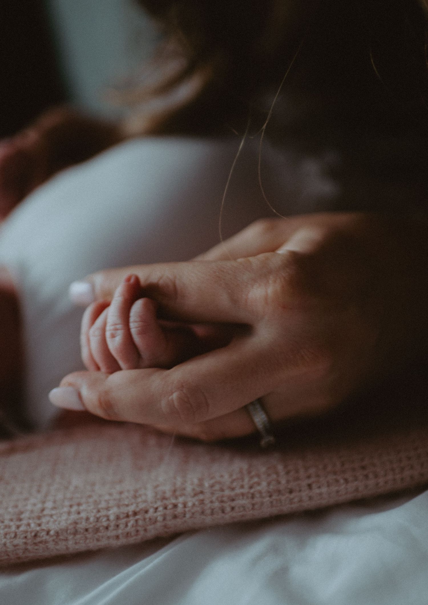 Close-up of mother holding tiny newborn baby hand on a pink knit blanket.