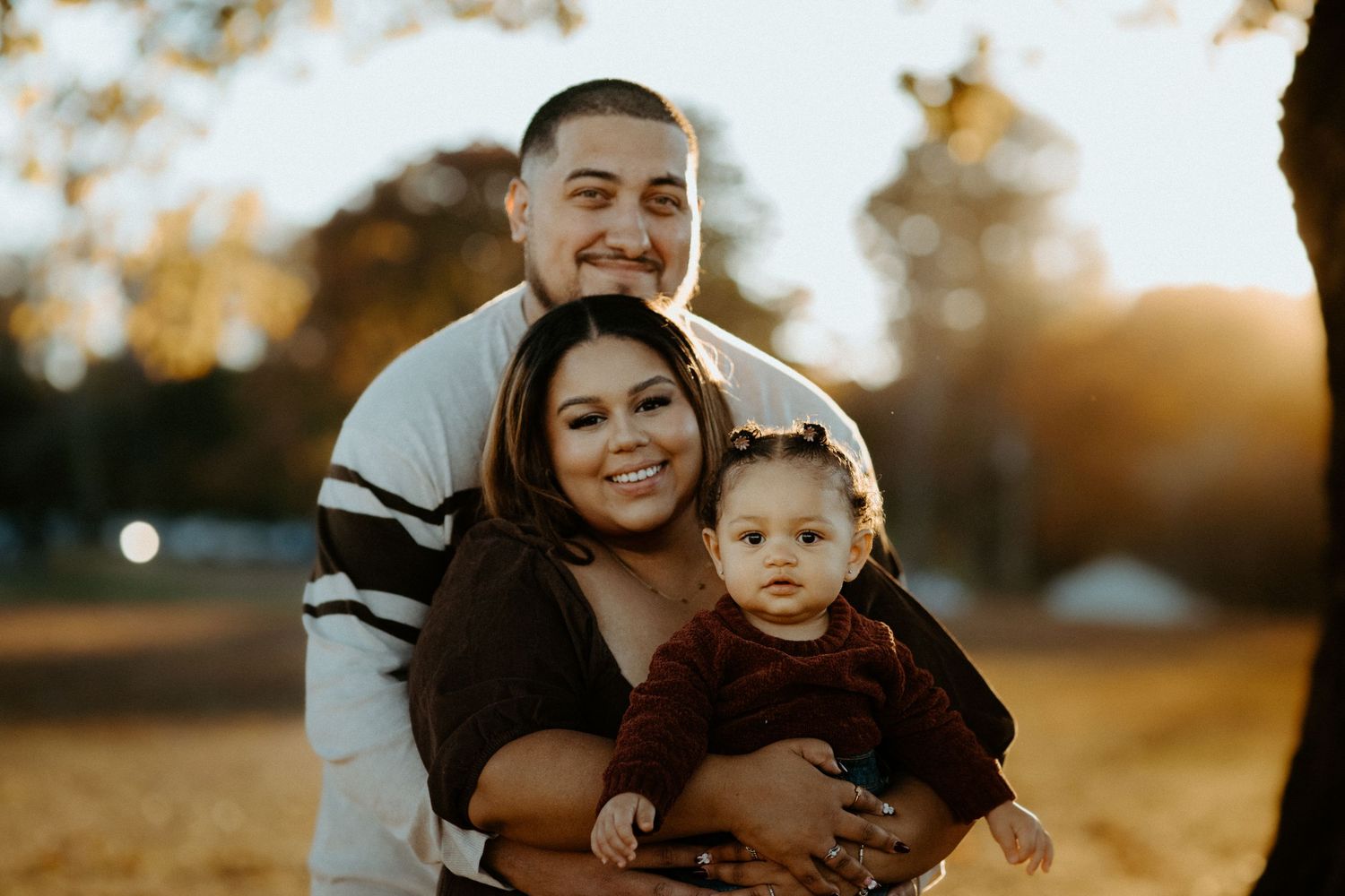 Family portrait with couple and baby smiling together in golden hour outdoor setting.
