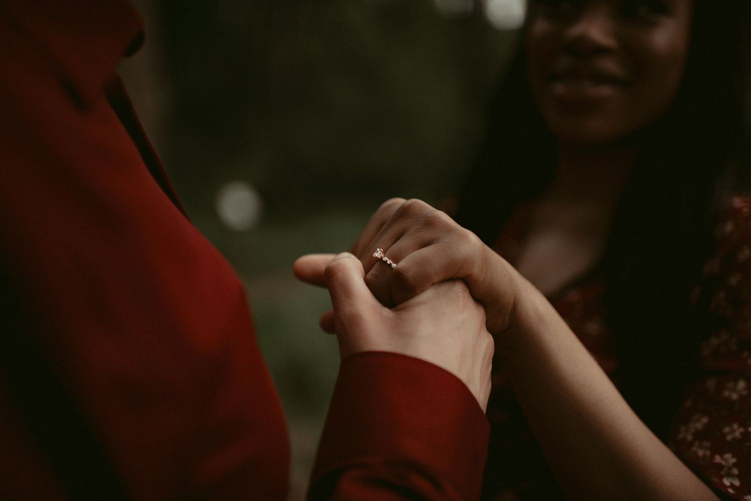 Romantic close-up of couple holding hands with a diamond engagement ring in an outdoor setting.