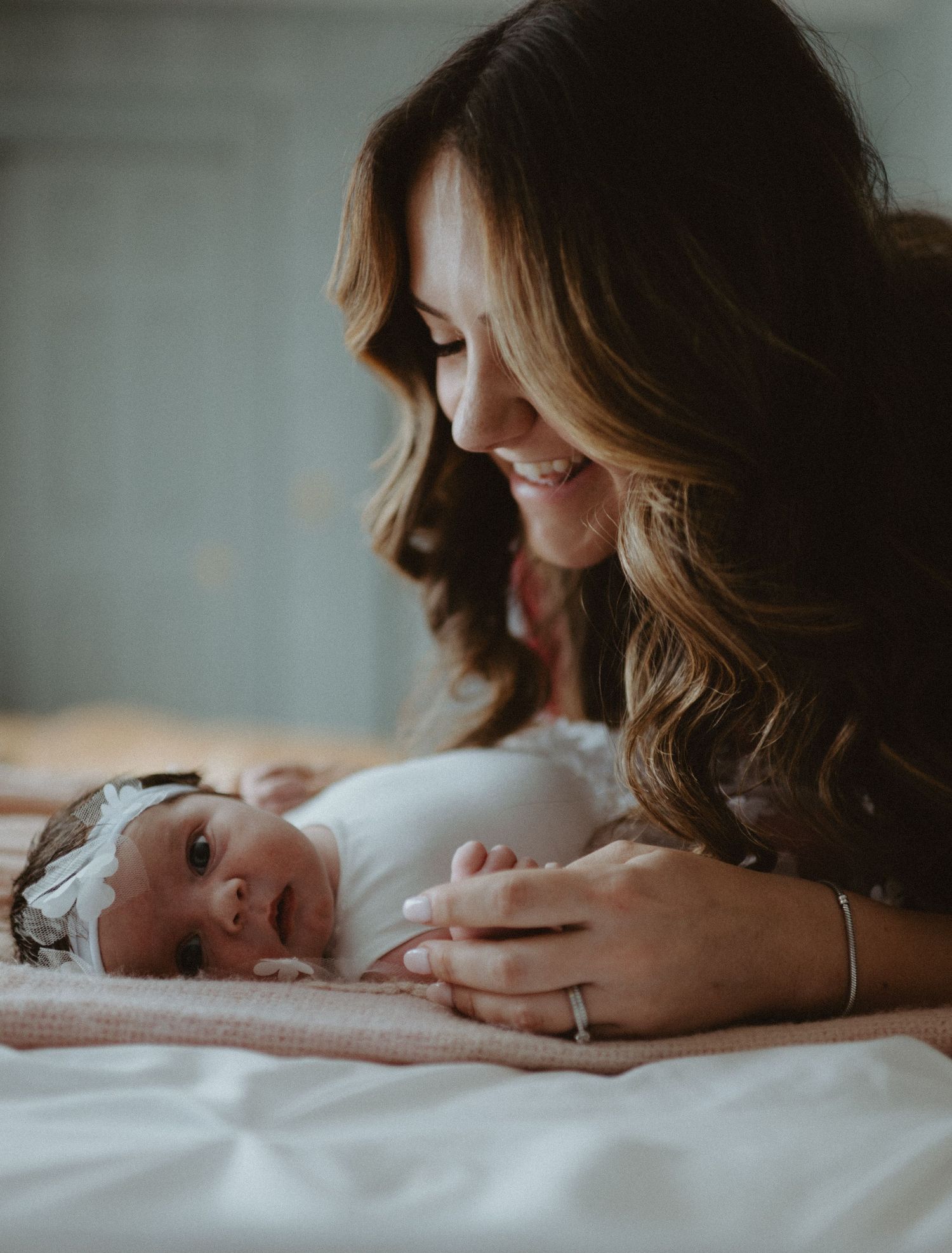 Smiling mother lying on bed gazing lovingly at her newborn baby wearing a floral headband.