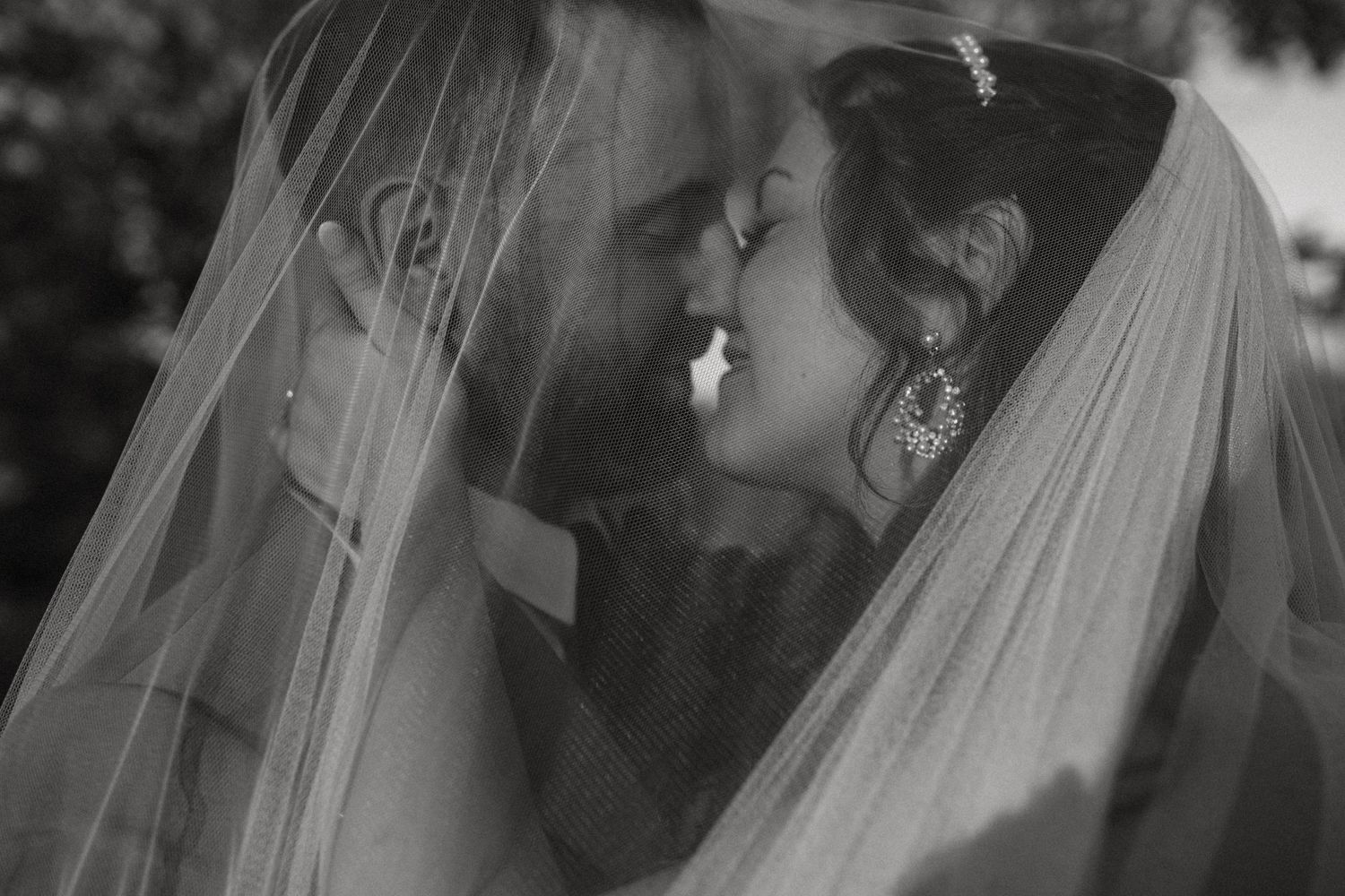 Romantic black and white wedding portrait of couple sharing a tender moment under a flowing bridal veil.