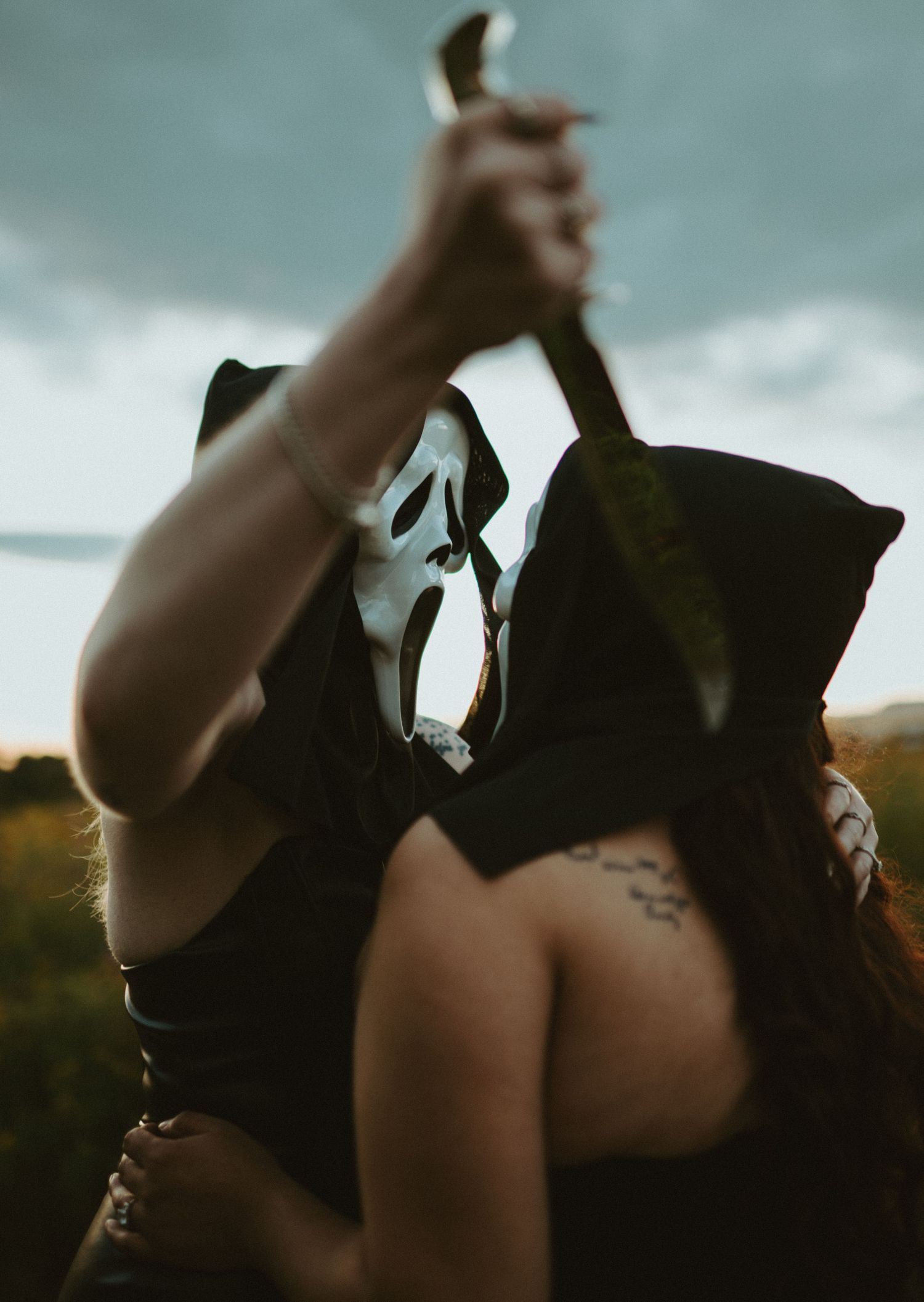 Person in Ghostface mask holding knife over victim in dramatic Halloween horror cosplay scene outdoors.