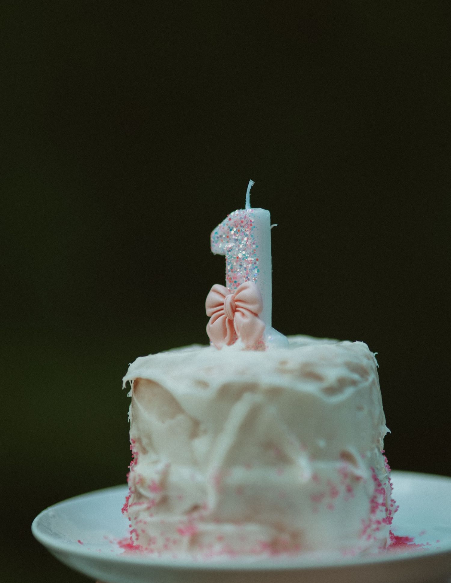 First birthday cake with white frosting and a glittery number one candle with pink bow.