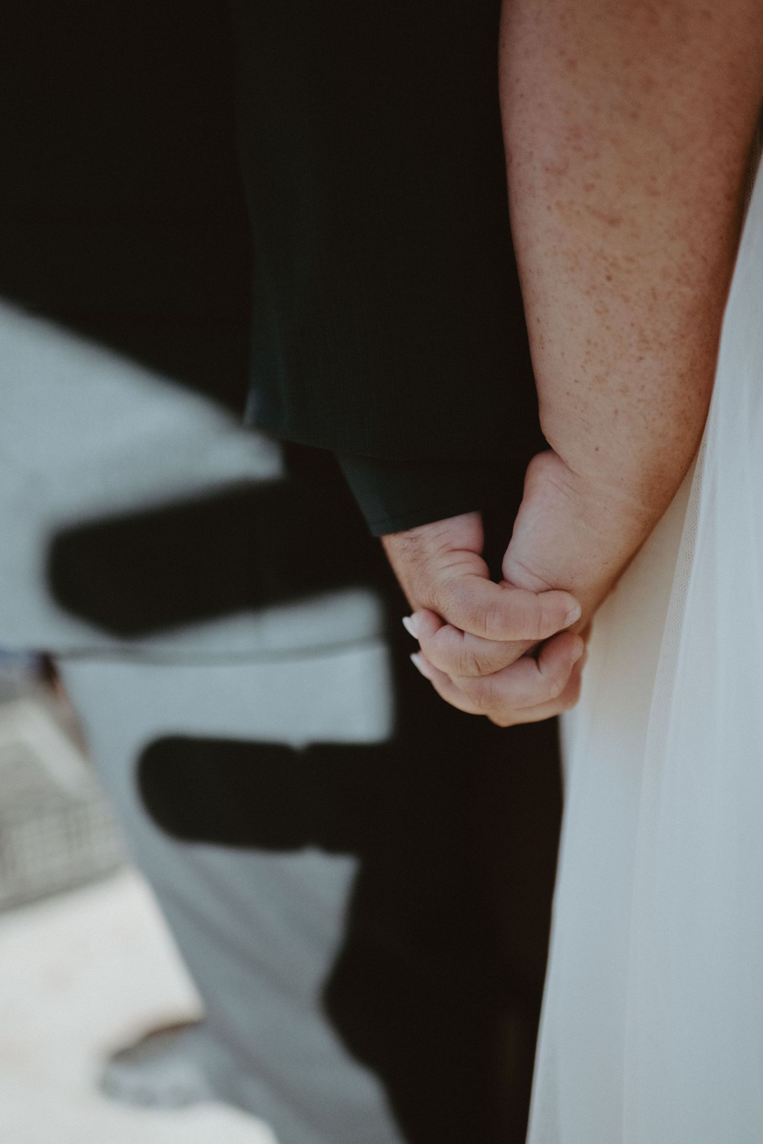 Close-up of a couple holding hands at their wedding, bride in white gown and groom in dark suit.