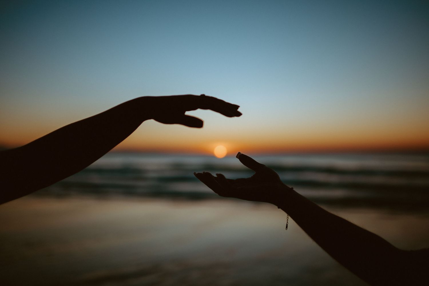 Silhouette of two hands framing the rising sun over a calm ocean at dawn on beach.