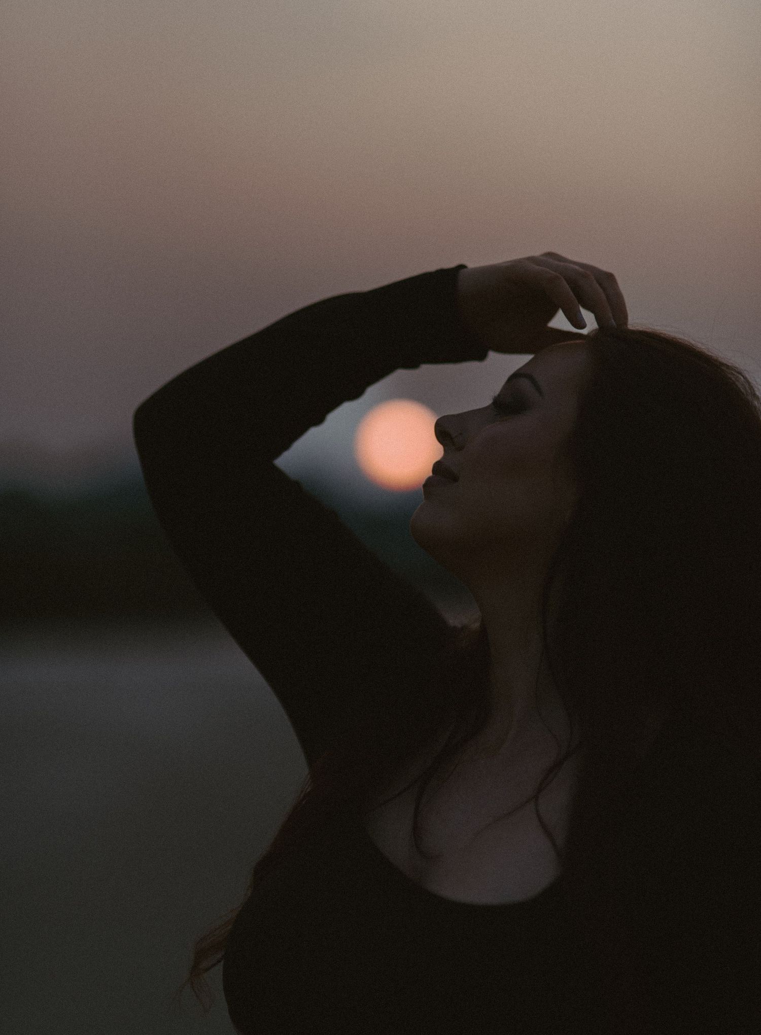 Artistic silhouette of woman posing against dawn sky with glowing sun rising behind her head.