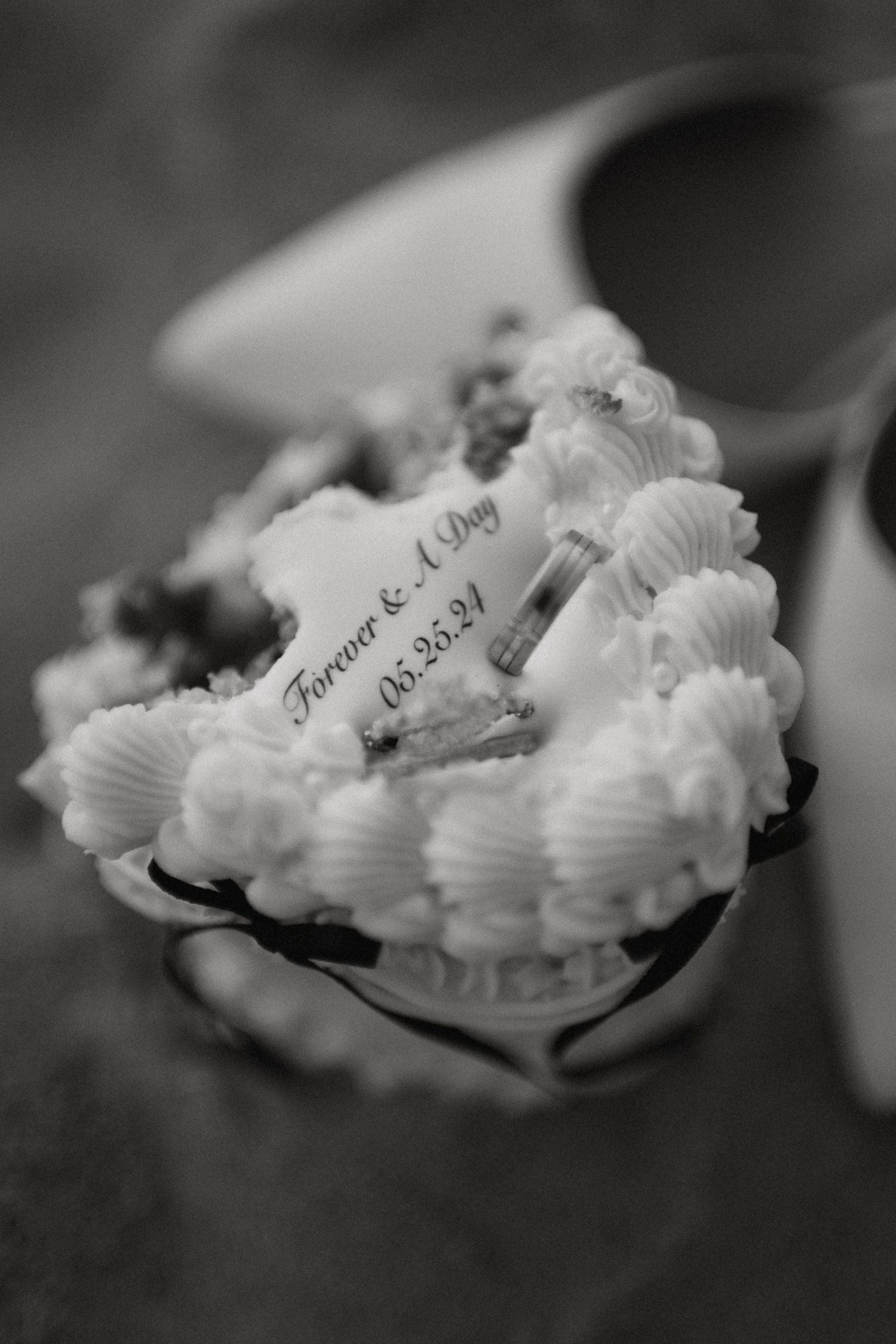 Black and white close-up of heart-shaped wedding cake topper reading Forever and A Day dated 05.25.24.