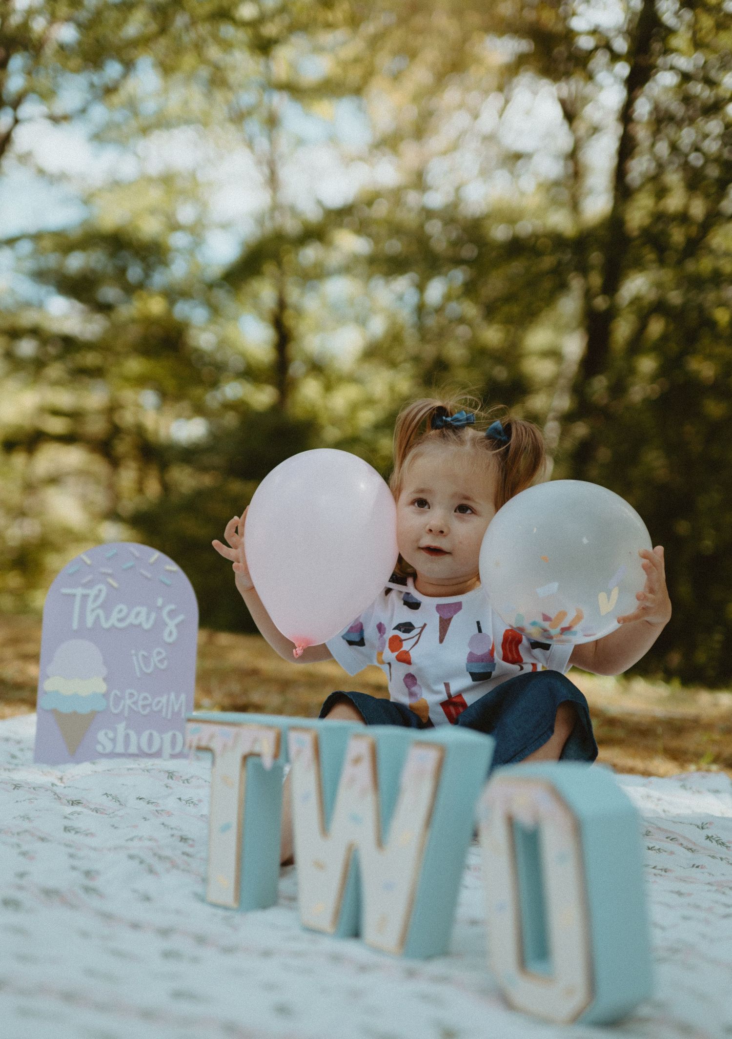 Toddler girl holding balloons beside TWO letters at birthday photo session.