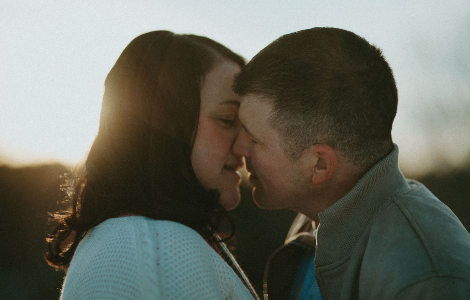 Couple sharing an intimate nose-to-nose moment bathed in warm golden sunset light.