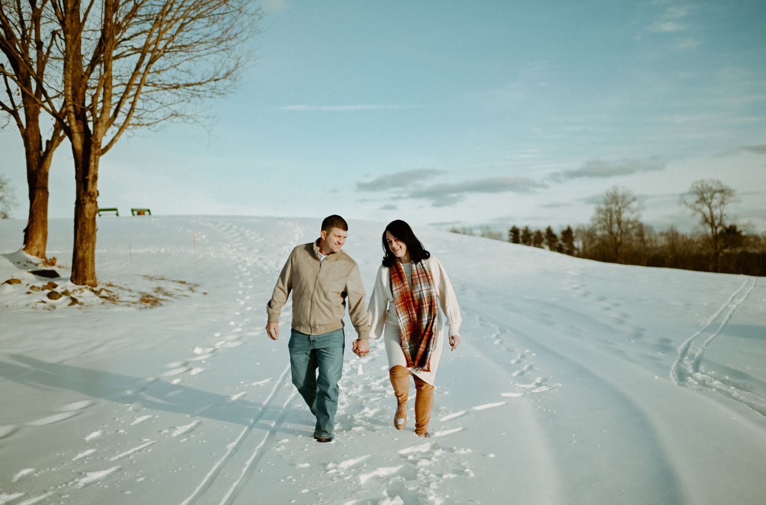 Couple holding hands and walking together along a sunny snow-covered country road in winter.