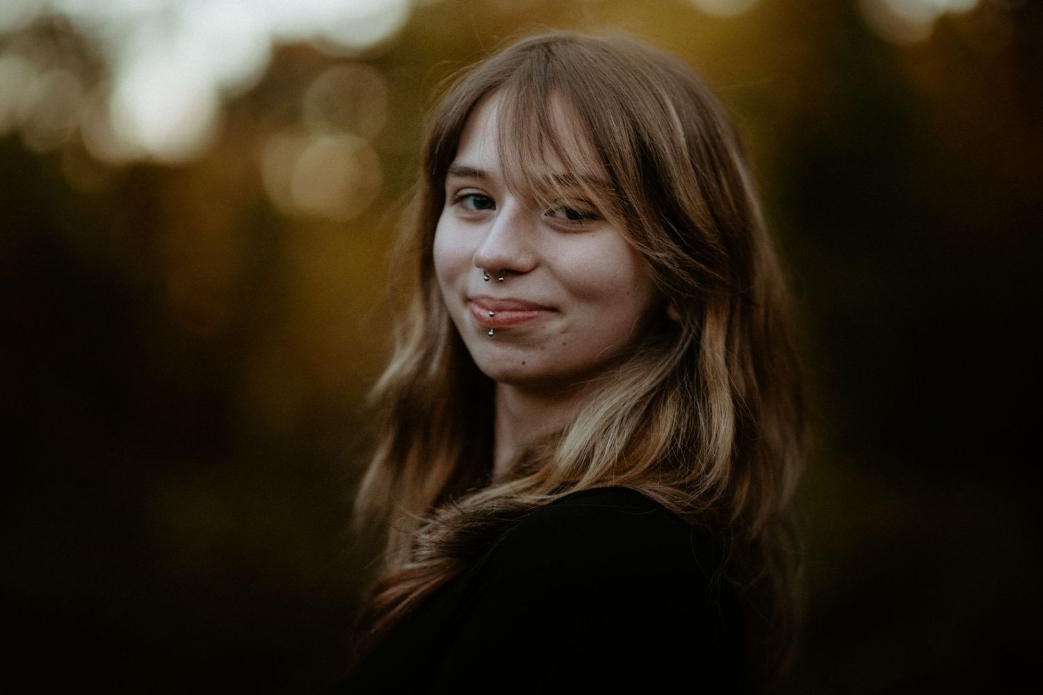 Young woman with wavy hair smiling over shoulder in golden autumn bokeh background.