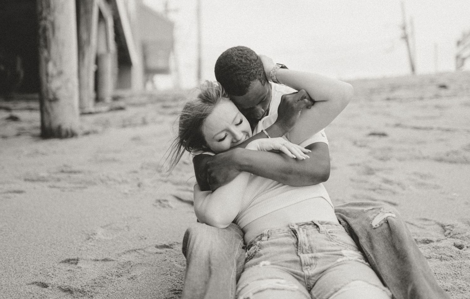 Black and white photo of a couple embracing while sitting on a sandy beach.