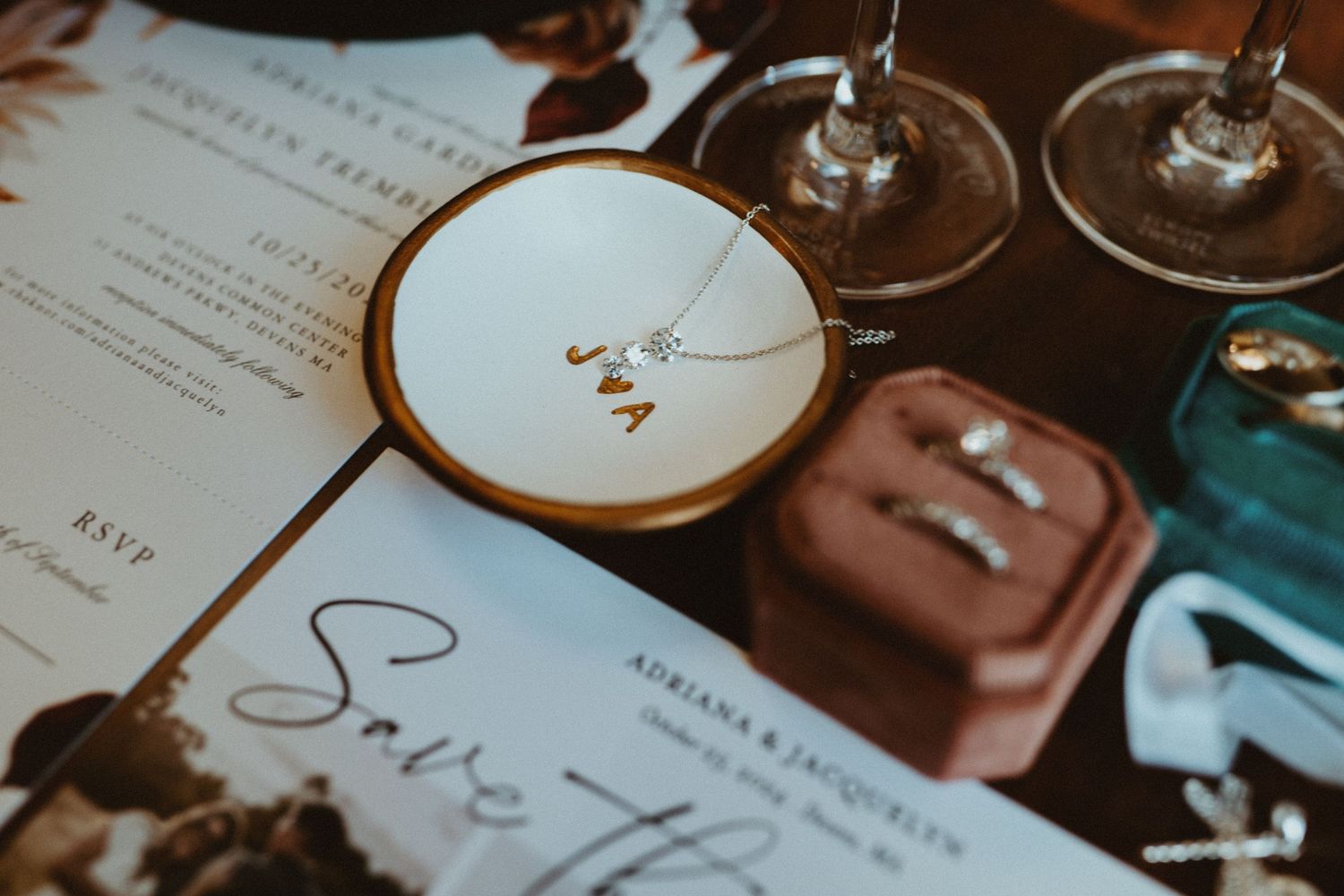 Elegant wedding flat lay featuring gold monogram jewelry dish, diamond rings, and save the date invitation cards.