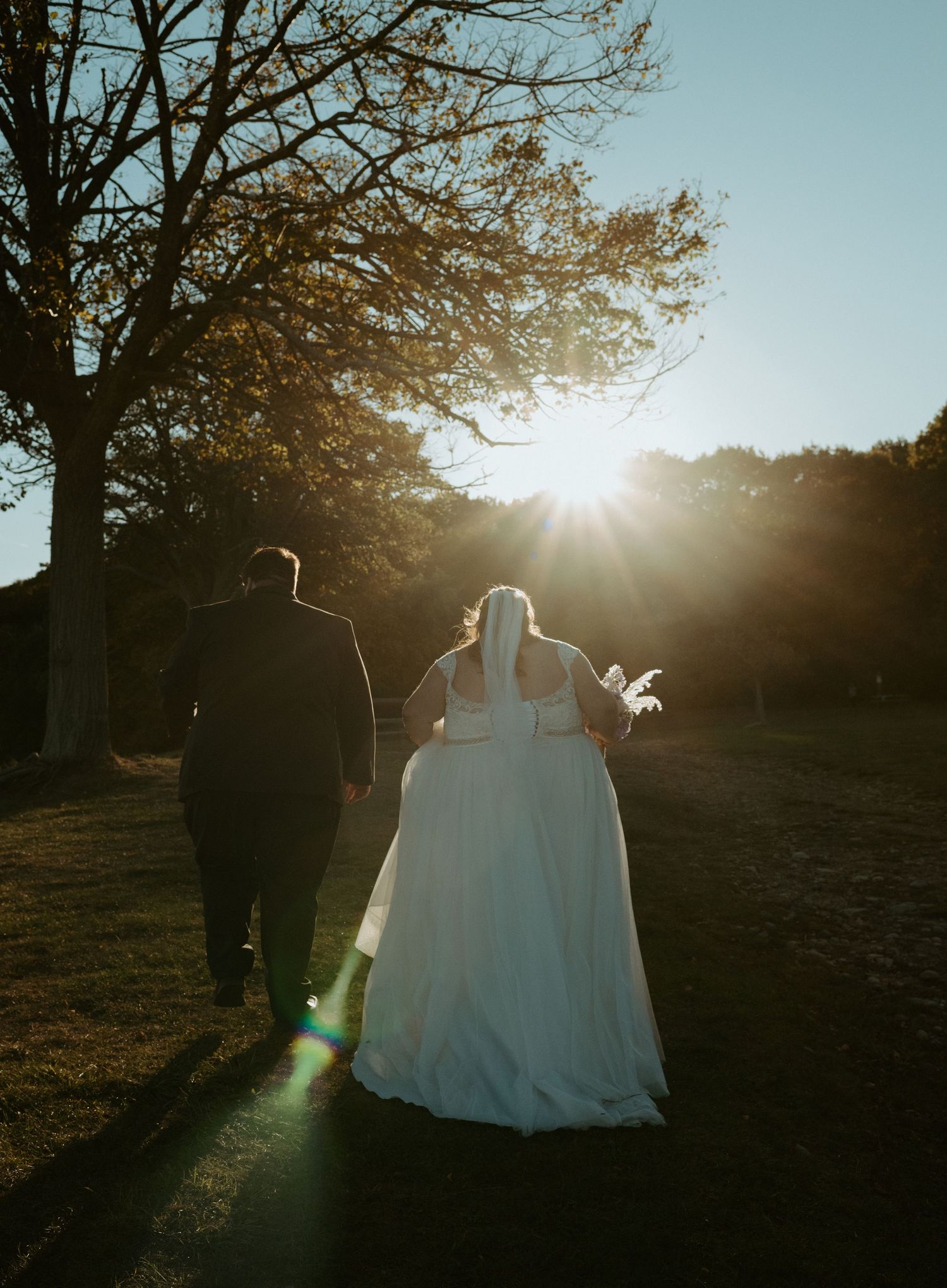 Bride and groom walking hand in hand toward golden sunset light in an outdoor garden setting.