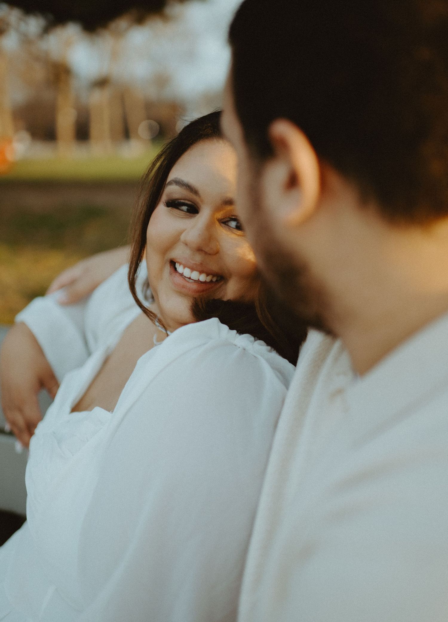 Woman in white dress smiling warmly at her partner during a golden hour outdoor engagement photo session.