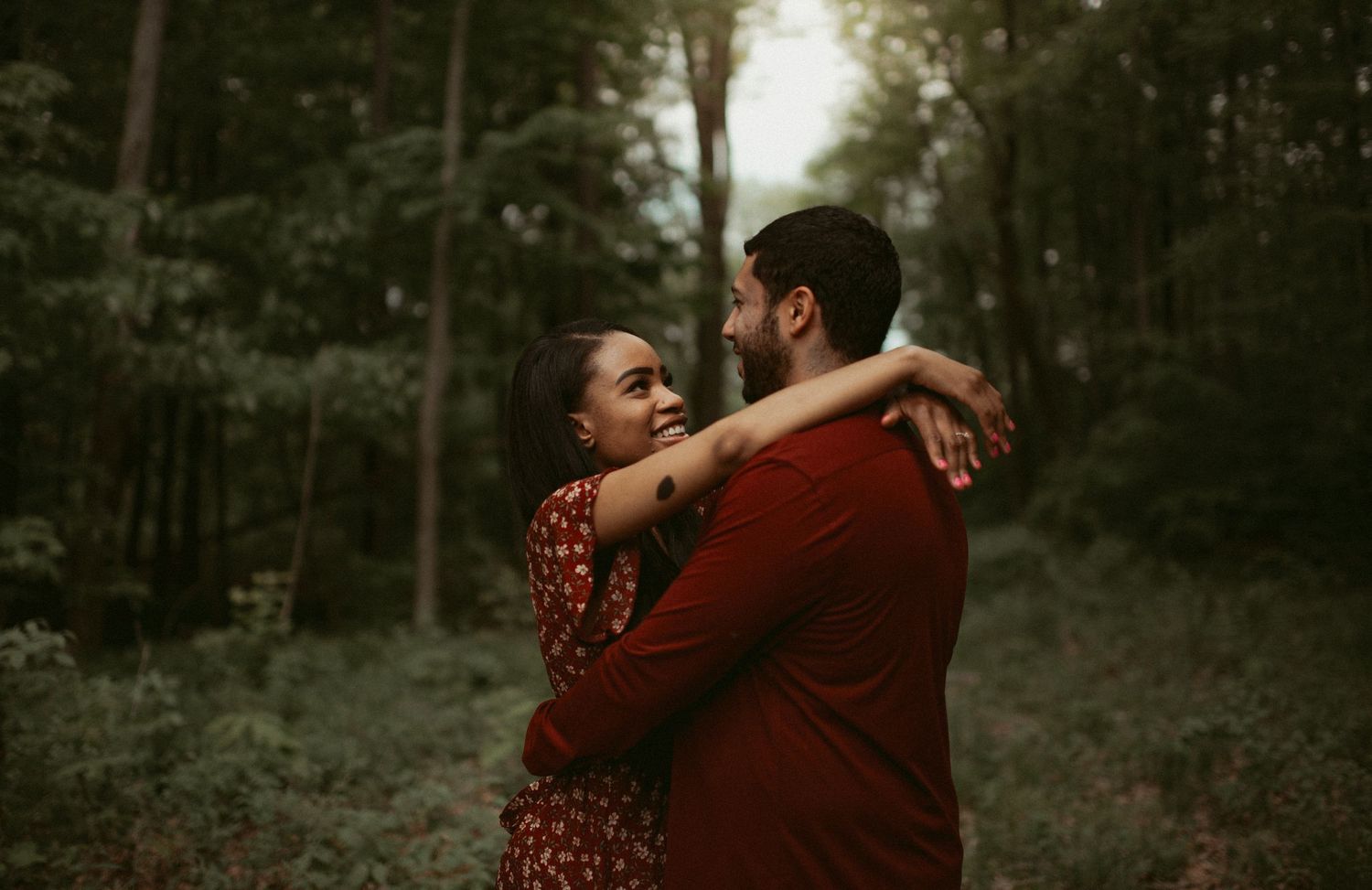 Happy couple embracing and smiling at each other in a lush green forest setting.