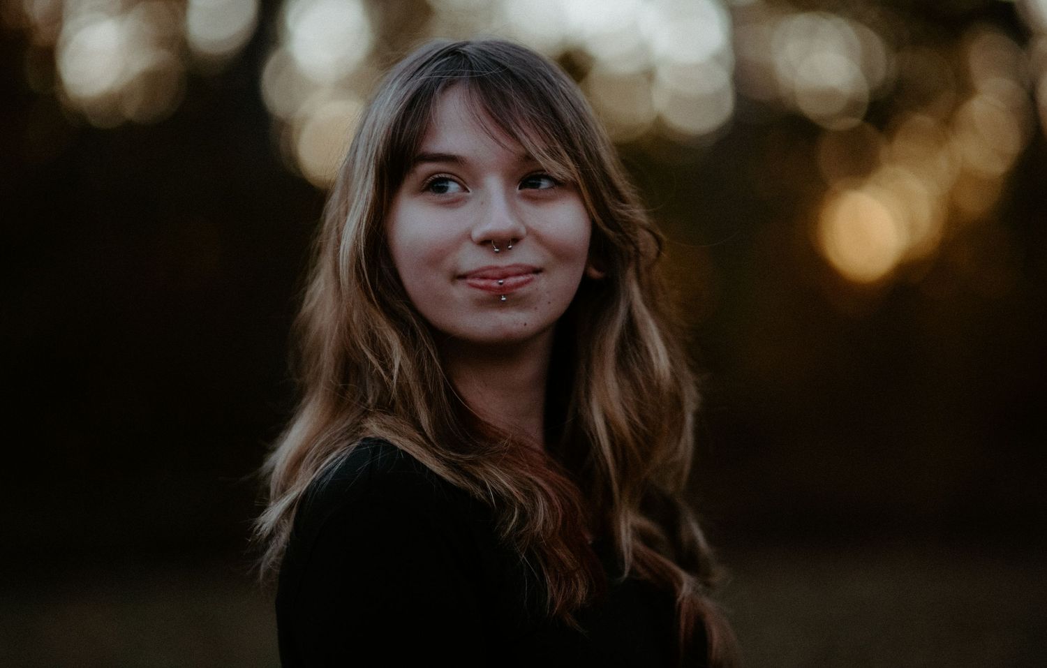 Young woman smiling softly outdoors in warm golden sunset bokeh light.