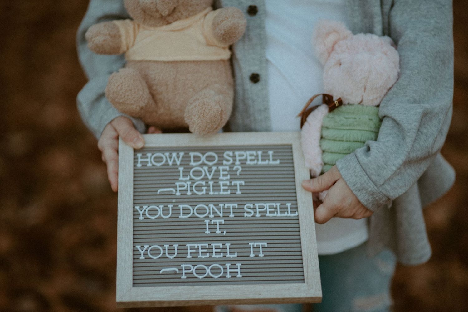 Pregnant woman holding Winnie the Pooh plush toys and letter board with Pooh love quote.
