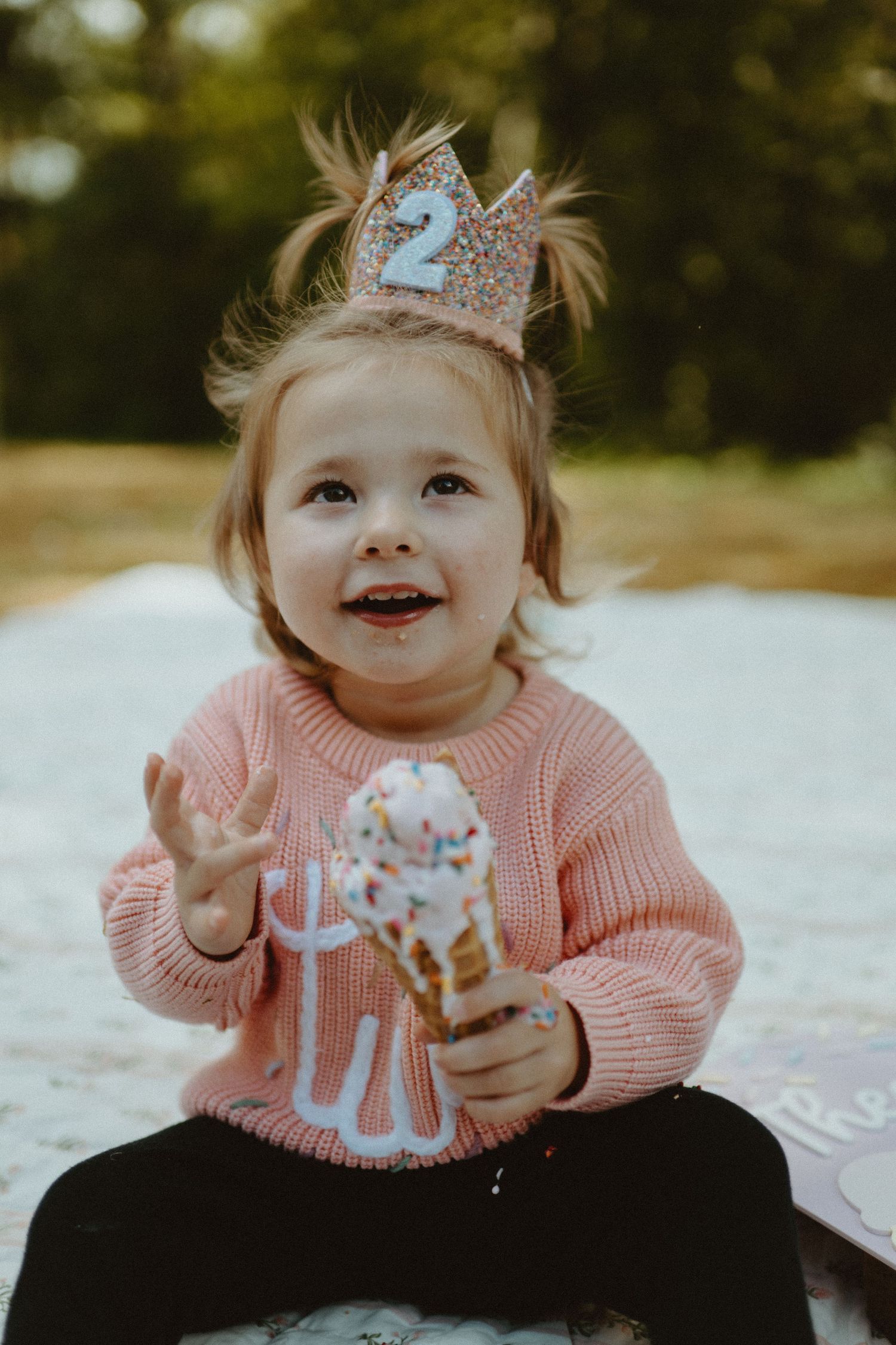 Happy 2-year-old girl wearing a glittery number 2 crown holding an ice cream cone.
