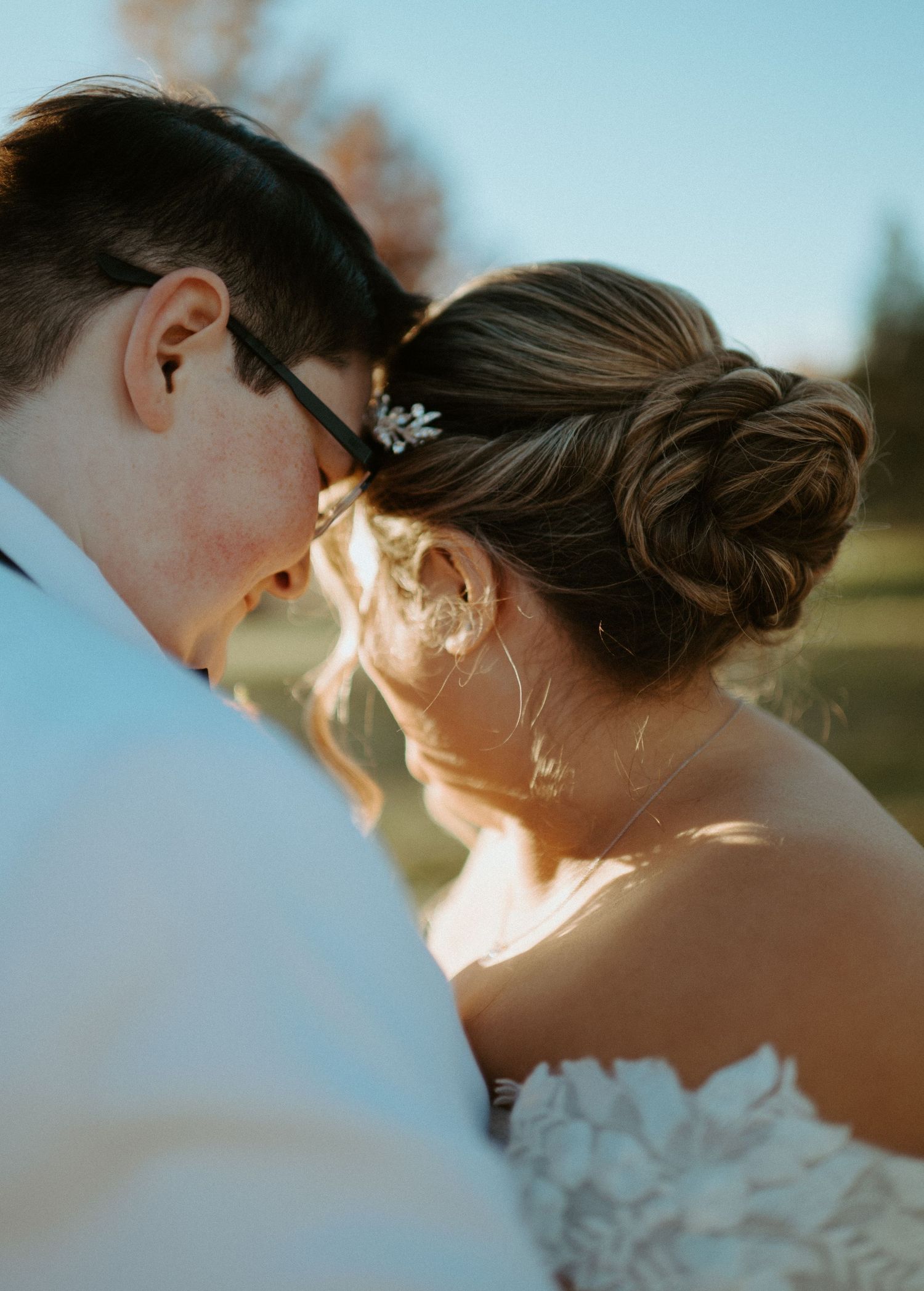 Intimate close-up of newlyweds touching foreheads with floral hair pin detail in warm light.