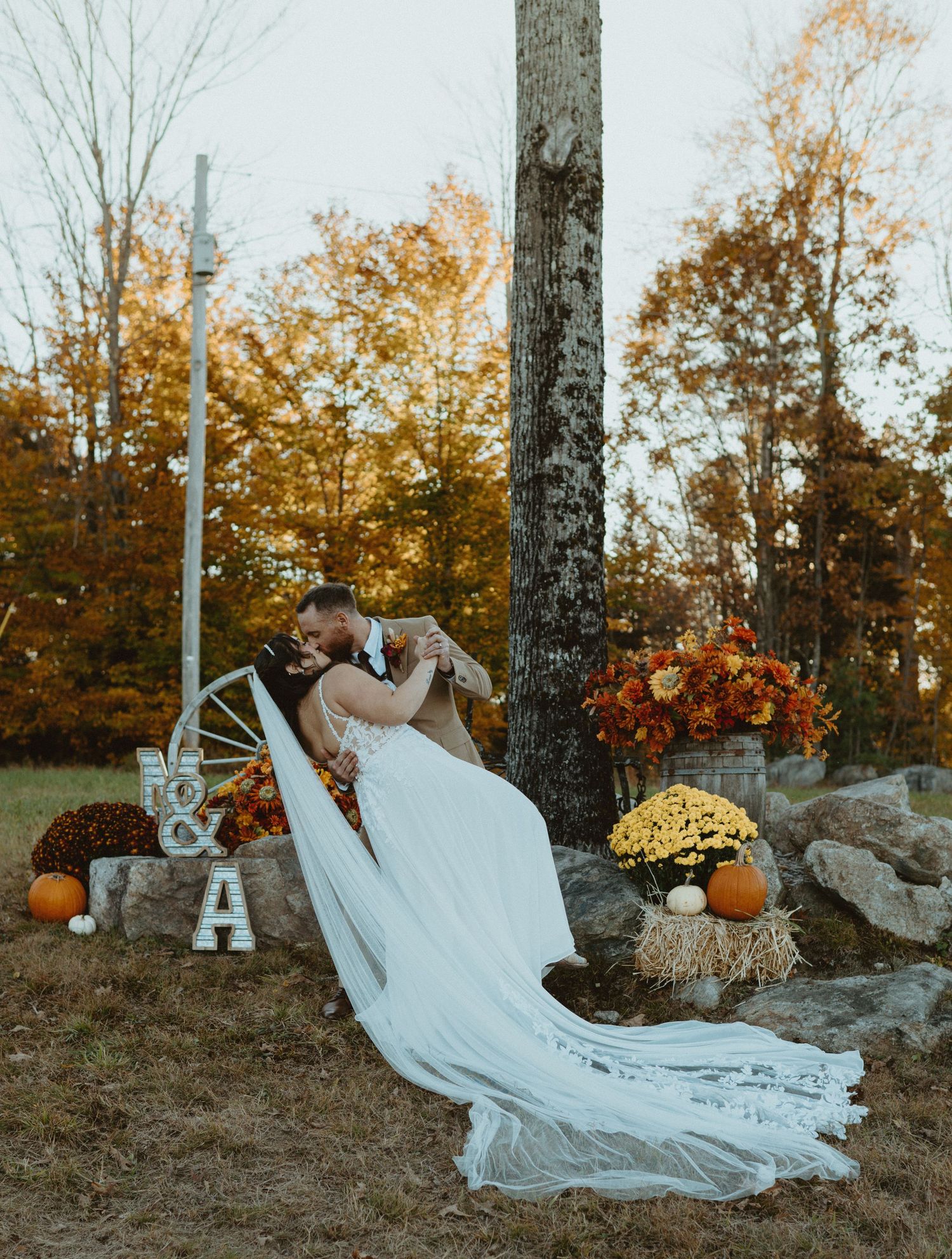 Couple sharing romantic dip kiss surrounded by fall pumpkins and autumn floral decorations.