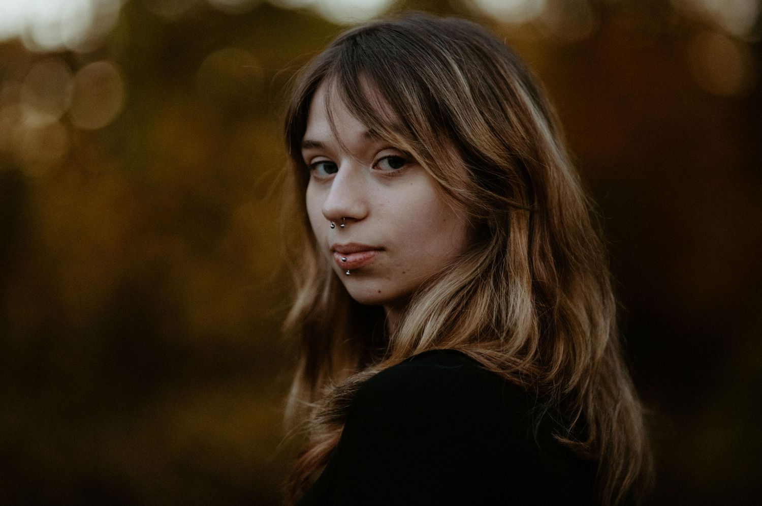 Young woman with wavy hair gazing at camera with soft autumn bokeh background.