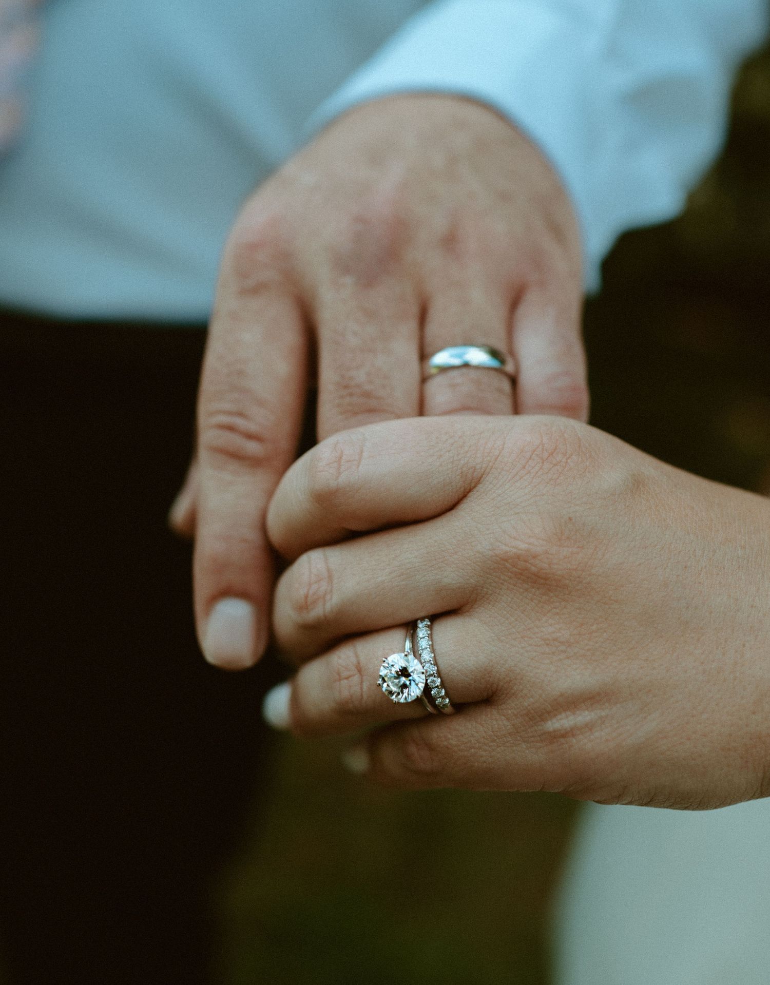 Close-up of couple holding hands showing diamond engagement ring, wedding band, and groom's ring.