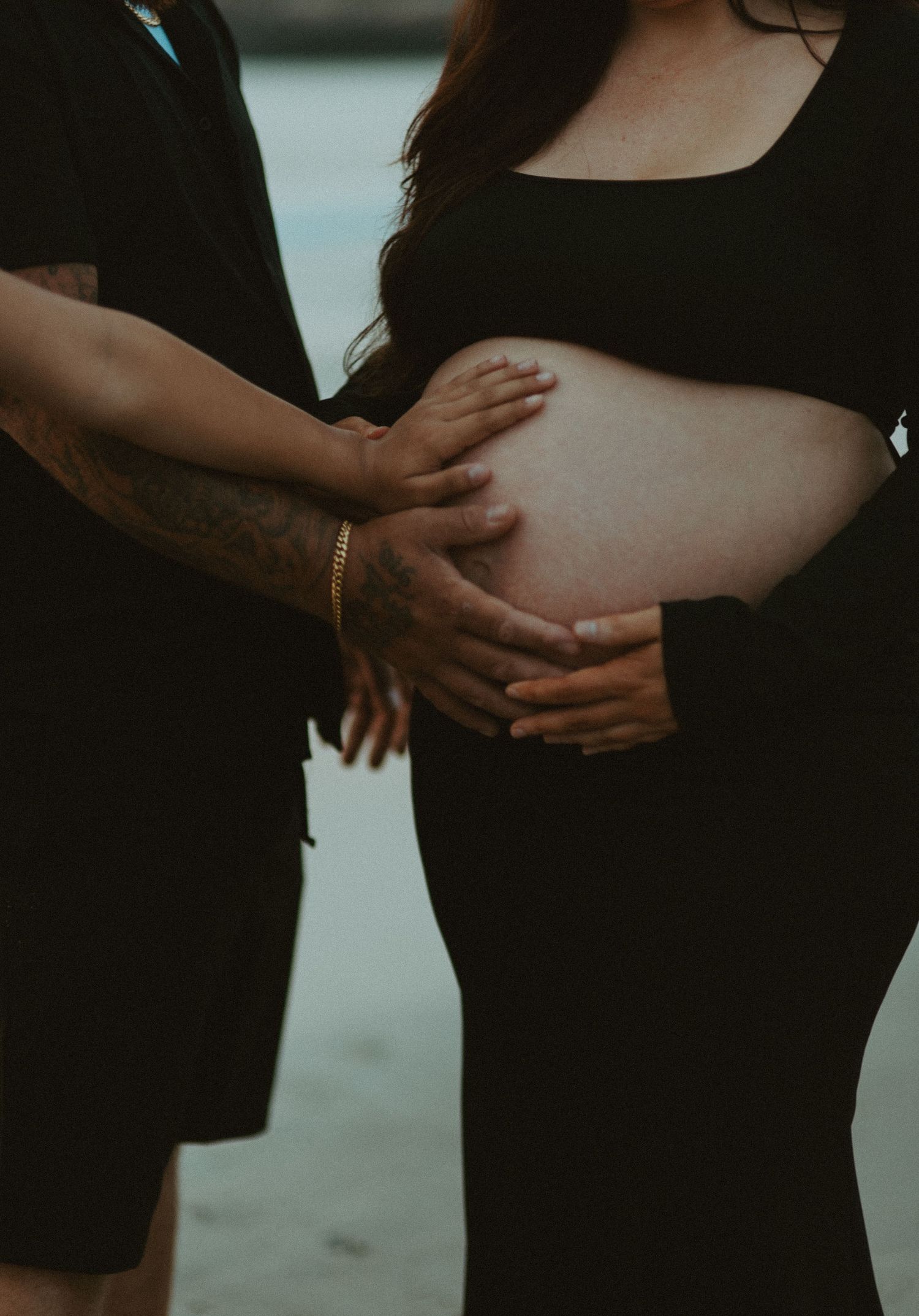 Close-up of couple lovingly cradling pregnant belly on a sandy beach.