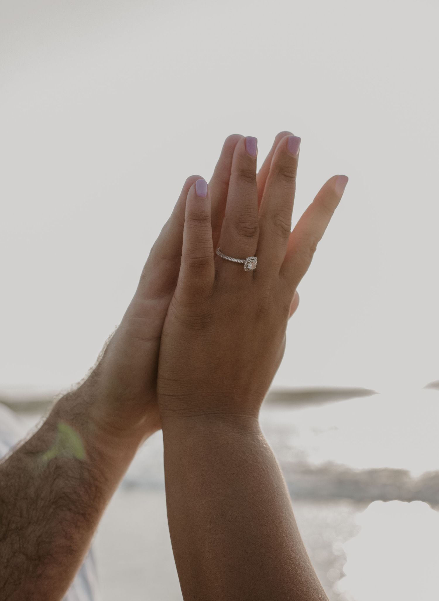 Close-up of hands touching with a elegant solitaire diamond engagement ring on womans finger.