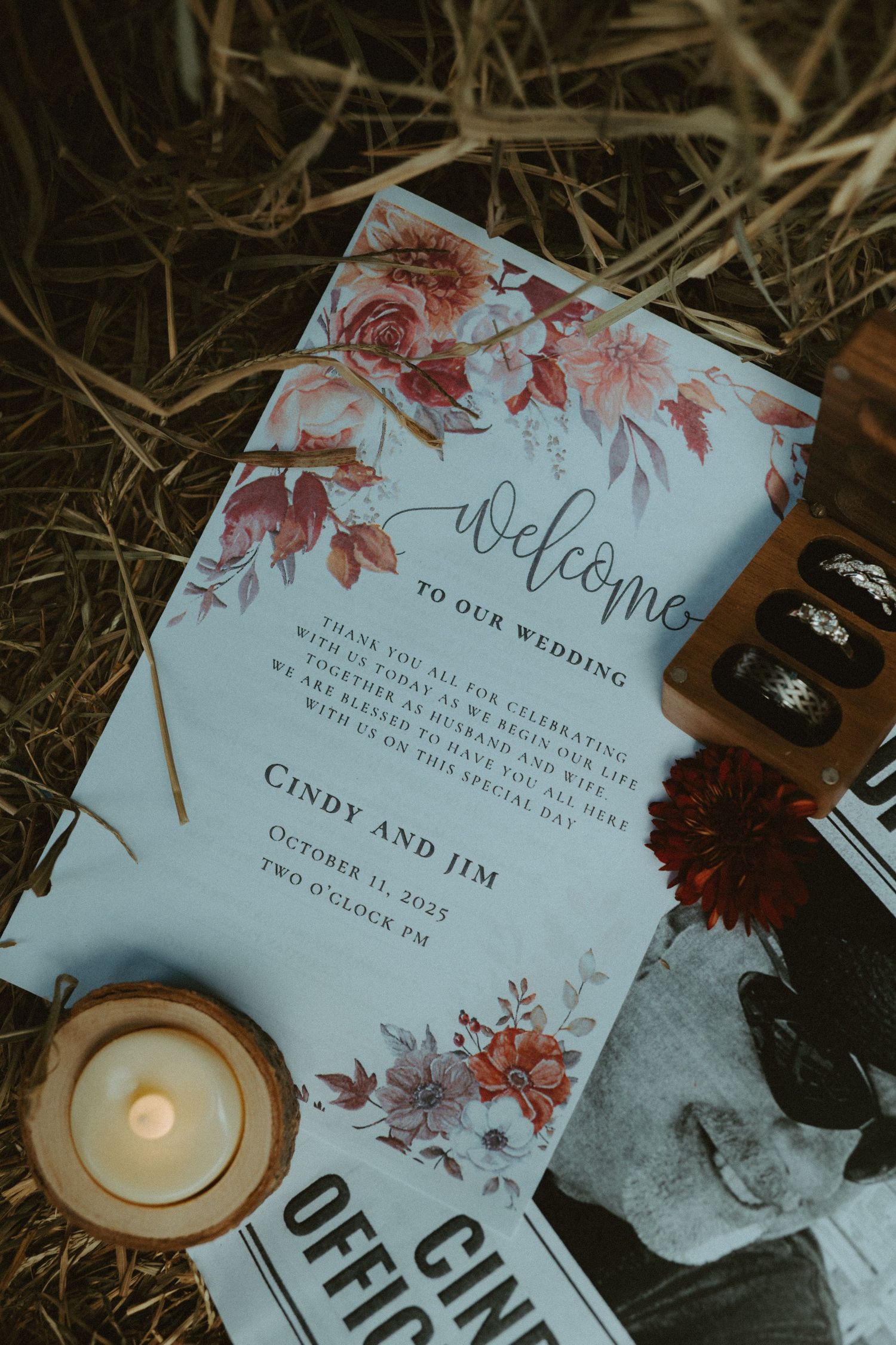 Wedding welcome sign for bride and groom with floral design displayed on hay with candle and rings.