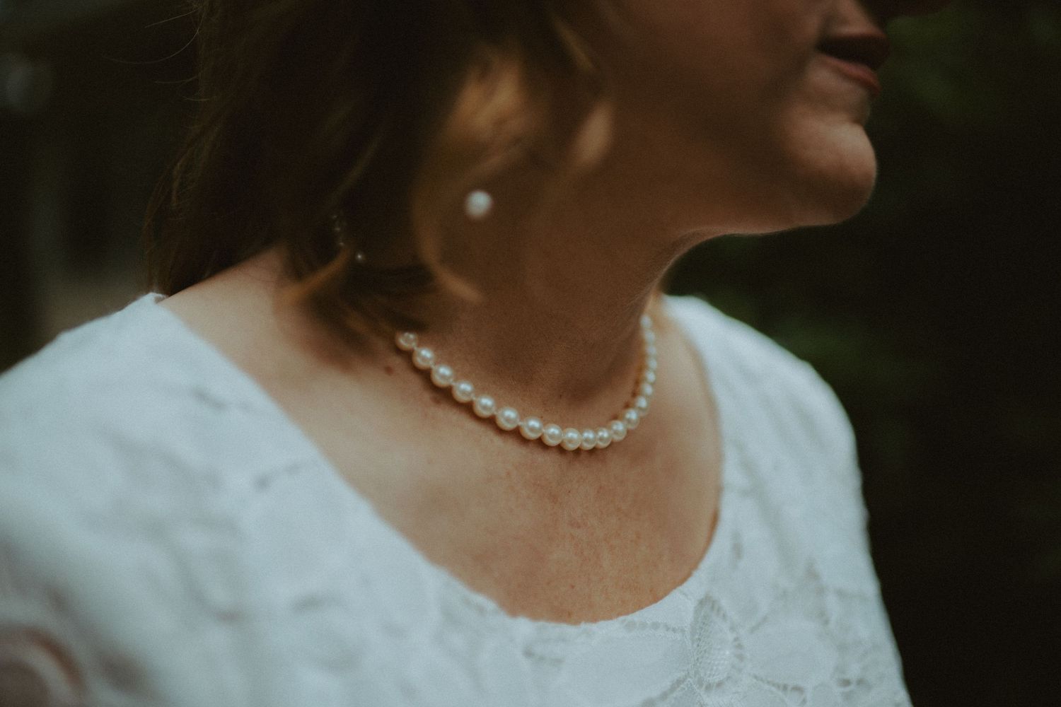 Close-up of bride wearing elegant pearl necklace and earrings with white lace wedding dress.