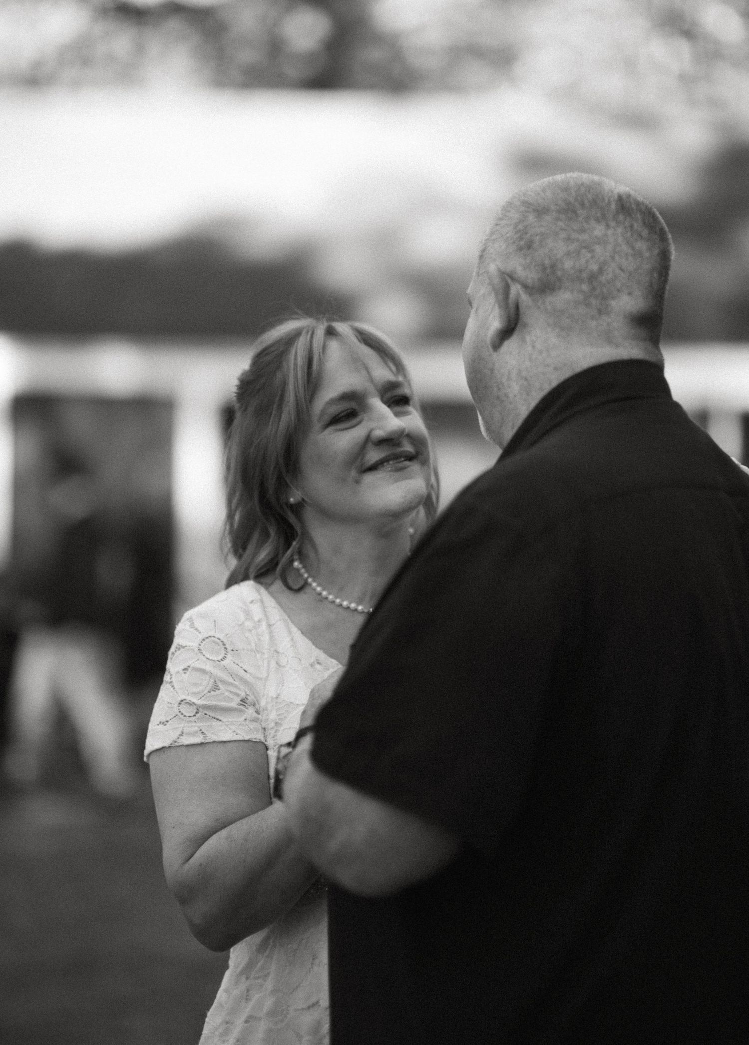 Black and white photo of newlyweds during first dance. Bride is smiling up at groom,