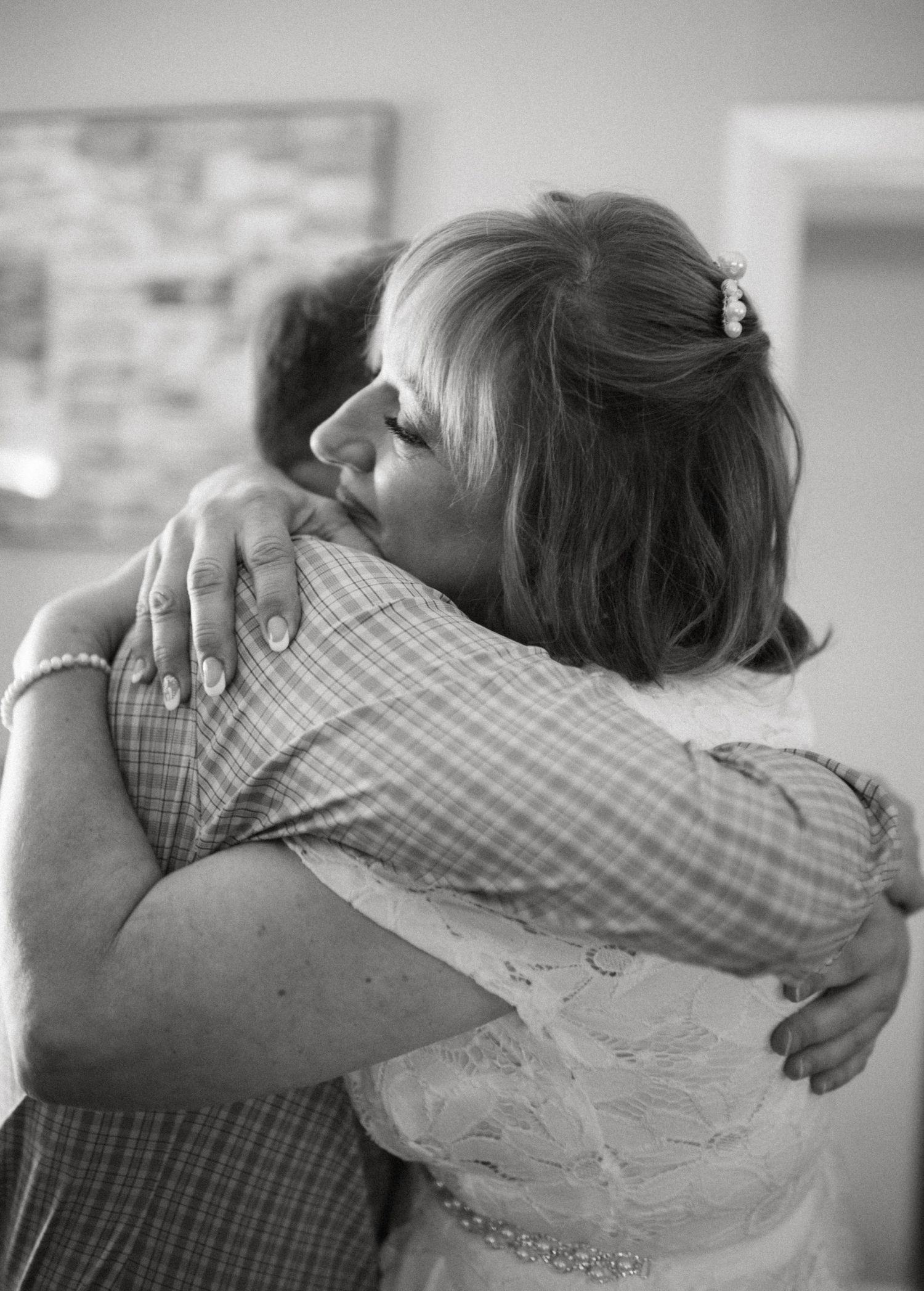 Black and white photo of emotional bride in lace gown sharing a warm embrace with relative.