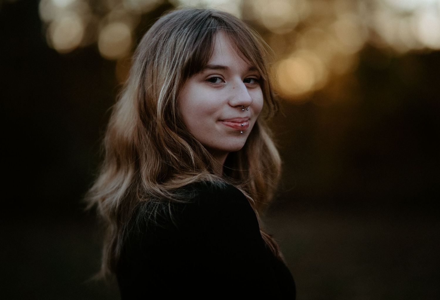 Young woman with wavy hair glancing over her shoulder with a subtle smile at golden hour outdoors.