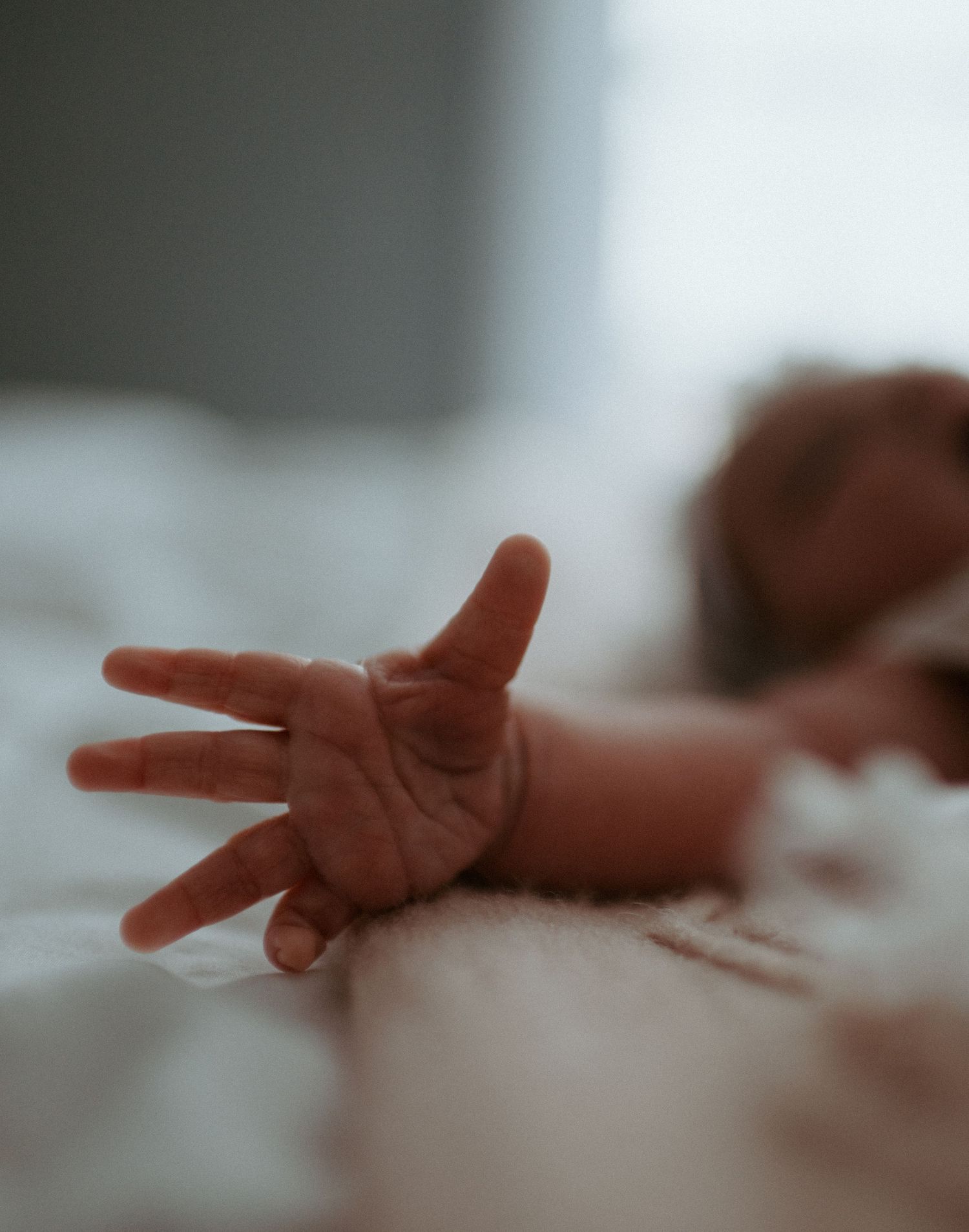 Delicate close-up of a newborn babys tiny outstretched hand resting on a soft white blanket.