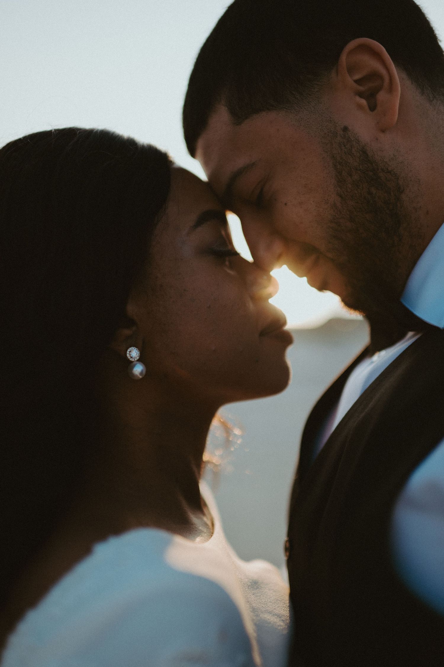 Romantic silhouette of bride and groom touching foreheads in intimate wedding portrait at sunset.