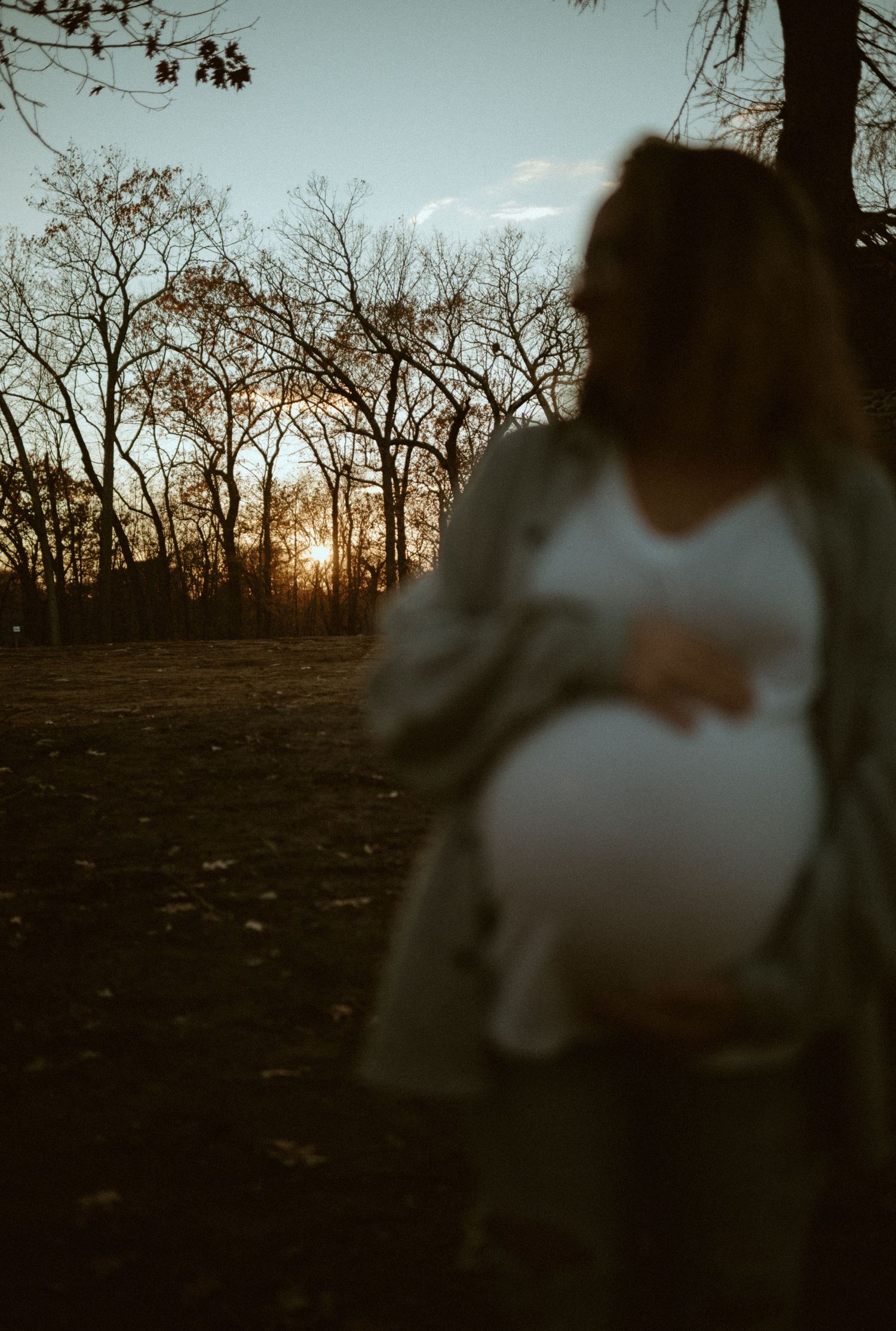 Pregnant woman holding belly at sunset in autumn park with bare trees.