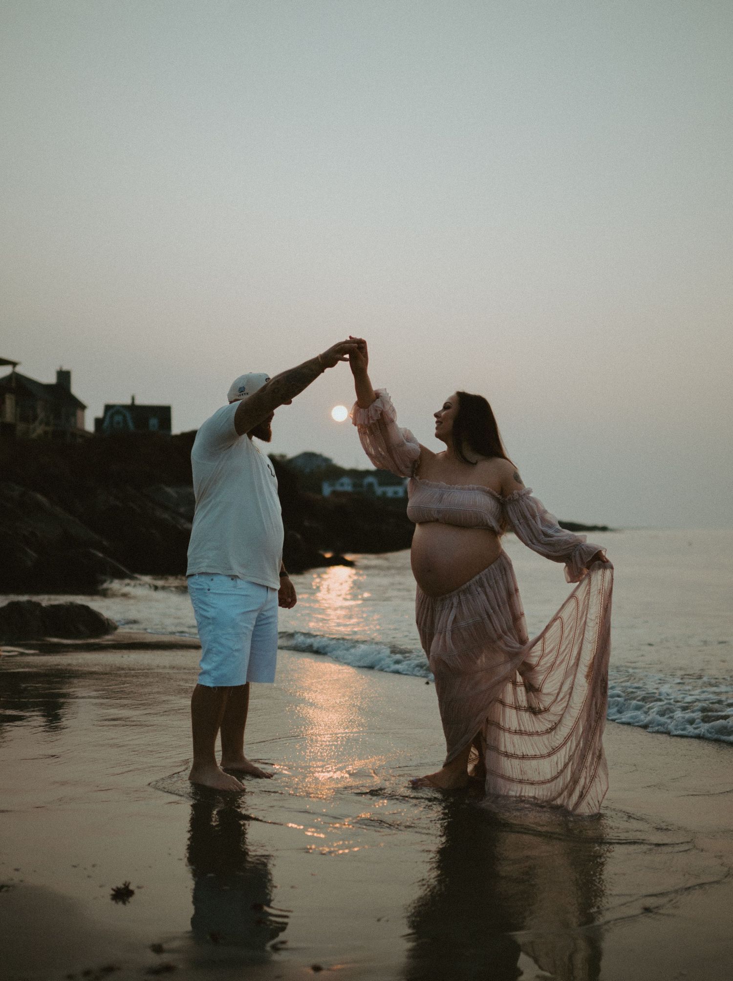 Couple dancing on a beach at sunrise. Woman is pregnant.