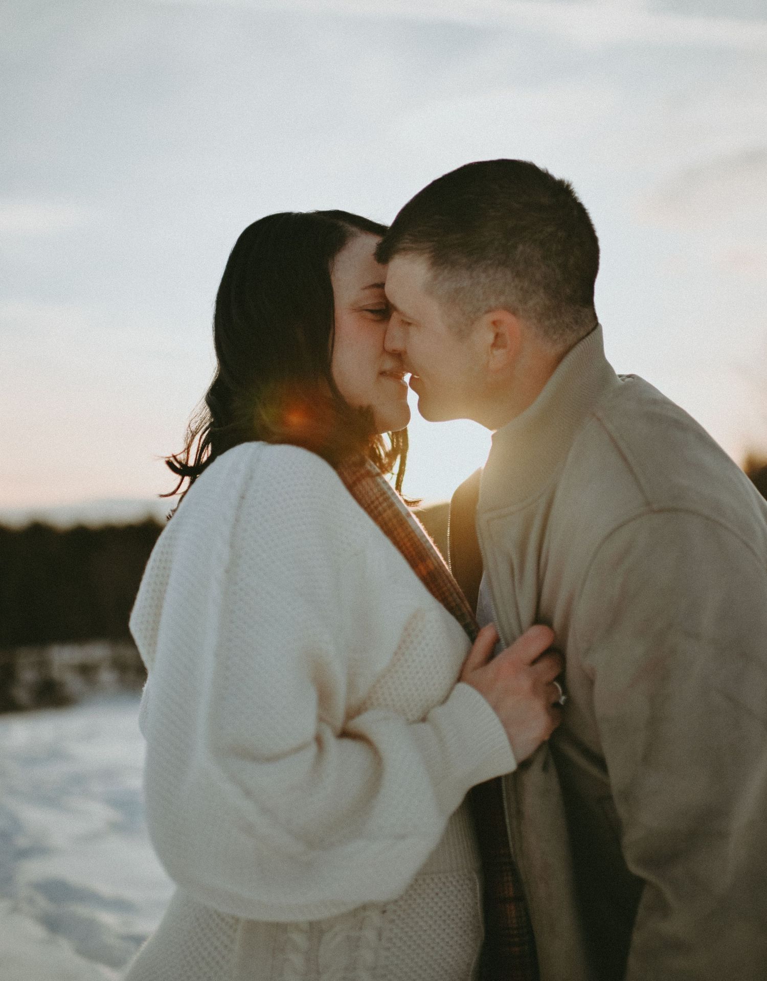 Romantic couple sharing a tender moment at sunset in a snowy winter landscape.