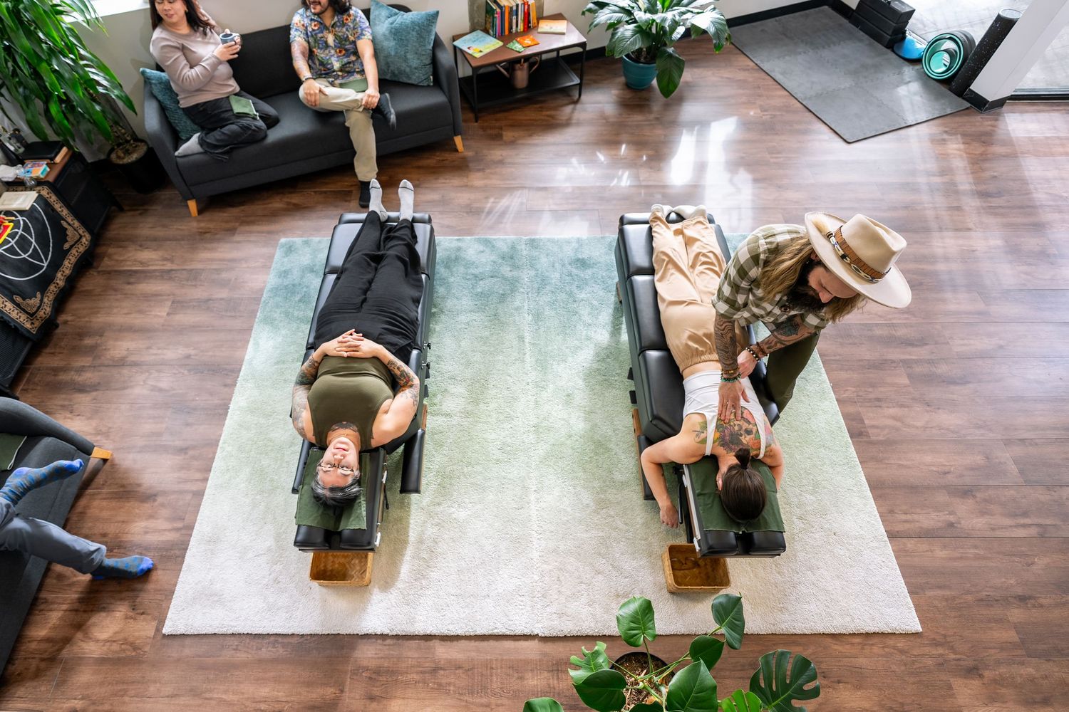 Aerial view of two people receiving wellness treatments on massage tables in a modern studio.
