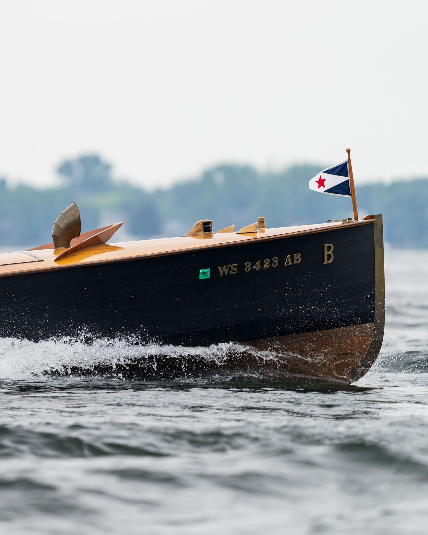 Classic wooden speedboat with registration WS 3423 AB cuts through choppy water, displaying a nautical pennant flag.
