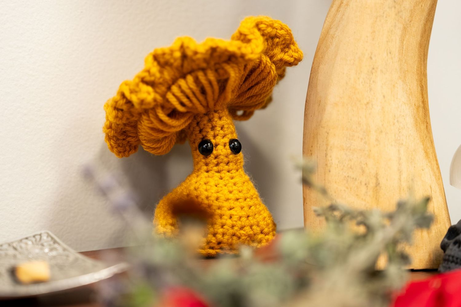 Handmade crocheted mushroom amigurumi toy in golden yellow yarn with googly eyes on a shelf.