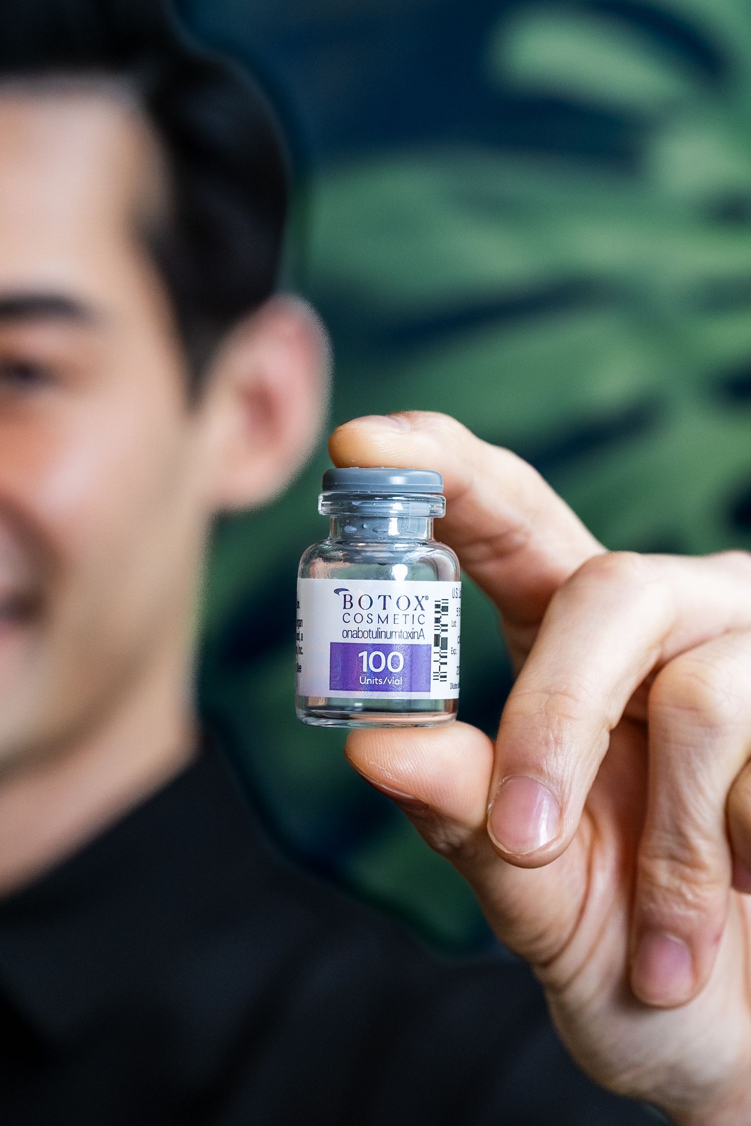 Healthcare professional holding a Botox Cosmetic 100 unit vial in focus against blurred background.