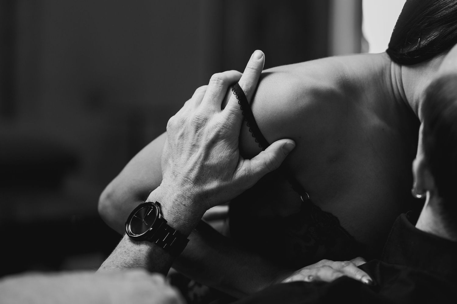 A close-up black and white image of hands with a watch embracing a bare back intimately.